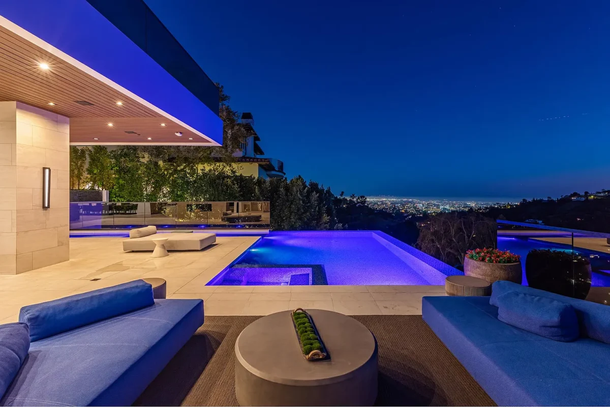 Twilight on the pool terrace, low sofas facing the lit infinity edge and the city grid below
