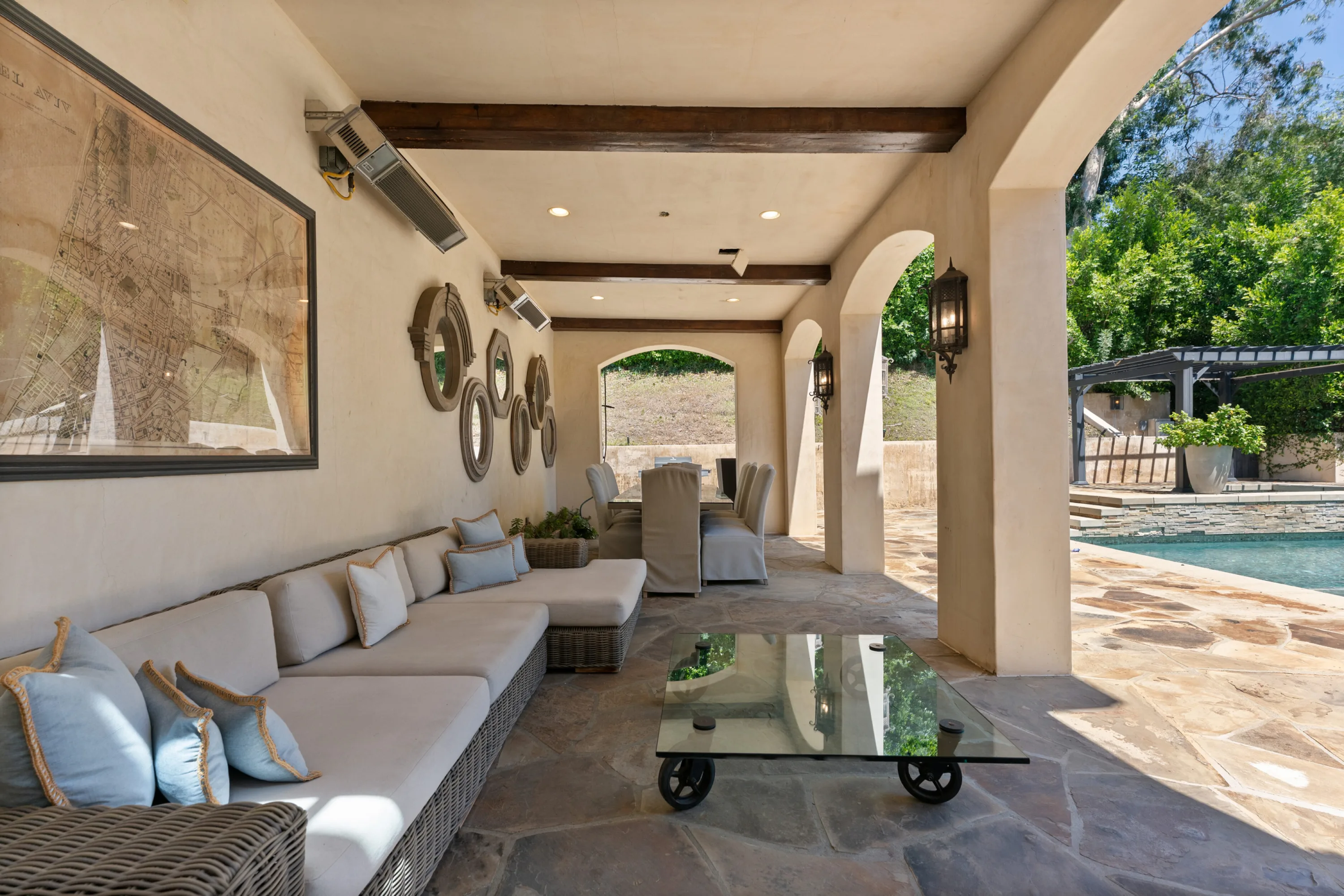 Covered loggia with wicker daybed seating, mirror-lined wall and outdoor dining beside the pool