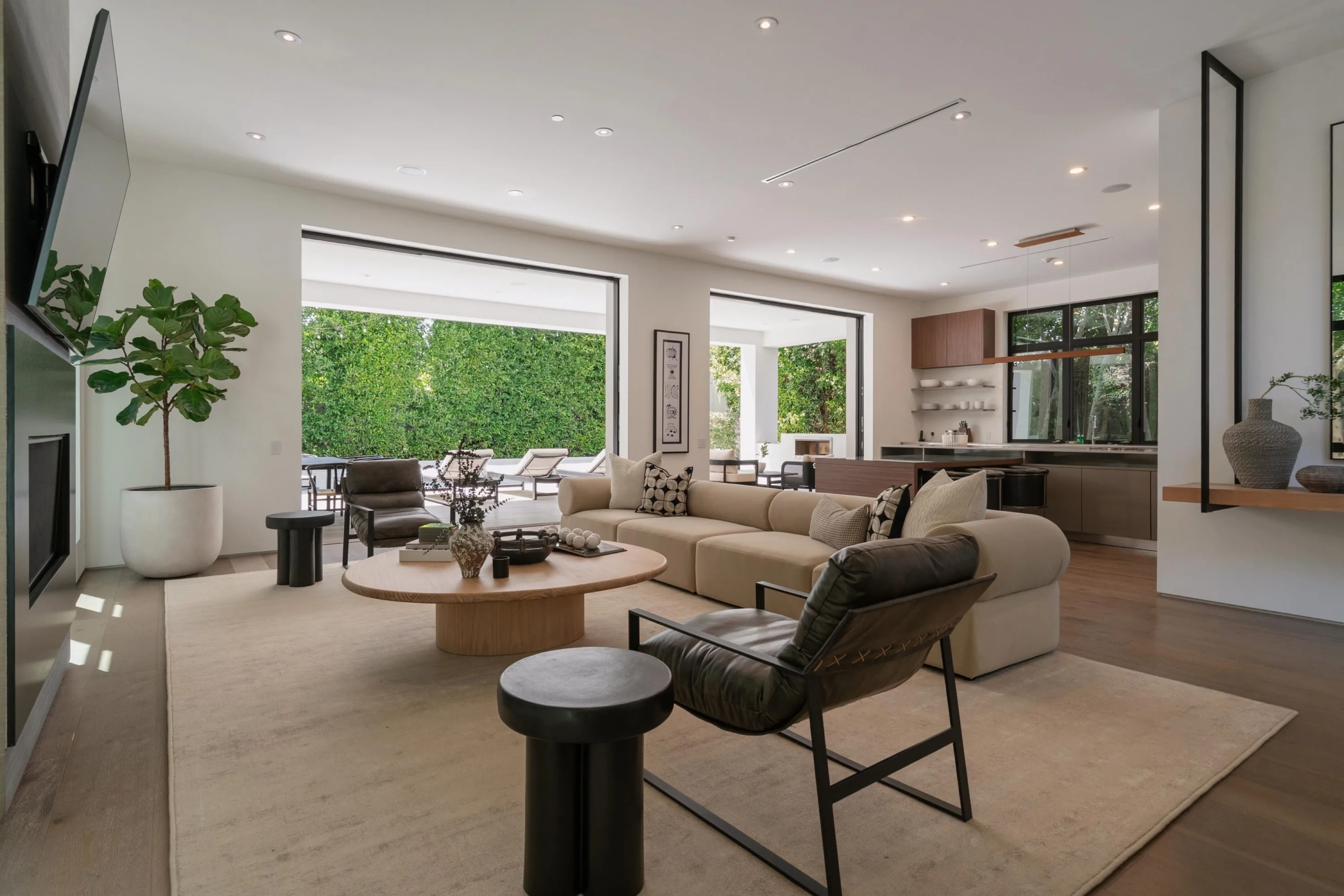 Open-plan living room with sliding glass walls retracted to the pool terrace and the kitchen beyond