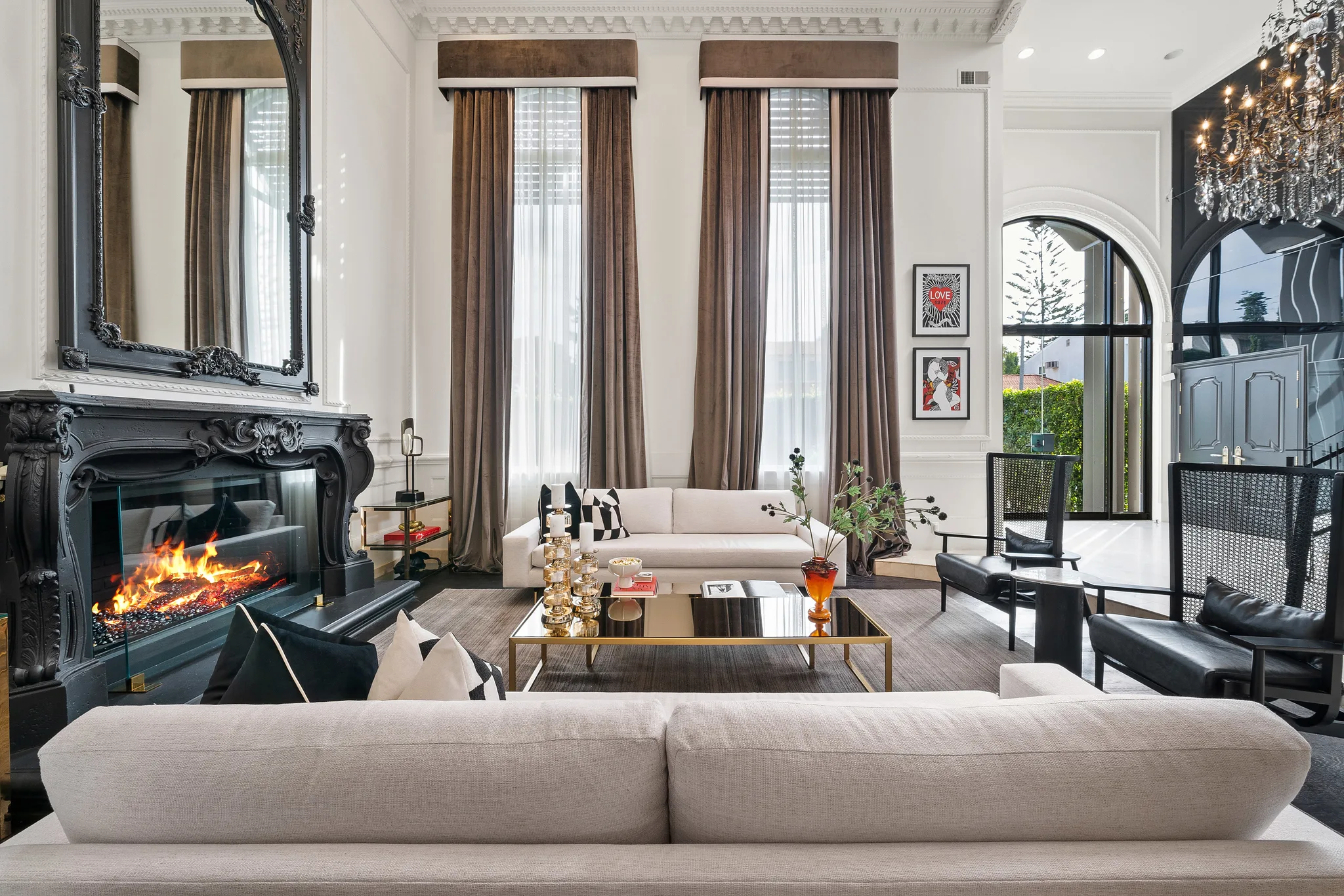 Double-height living room with lit black marble fireplace, cream sofas and floor-to-ceiling velvet curtains