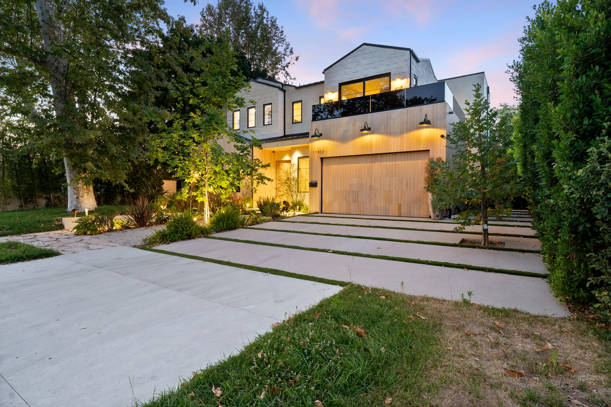 Villa Madison's lit facade at dusk, with oak garage door, sconces and a banded concrete driveway through lawn