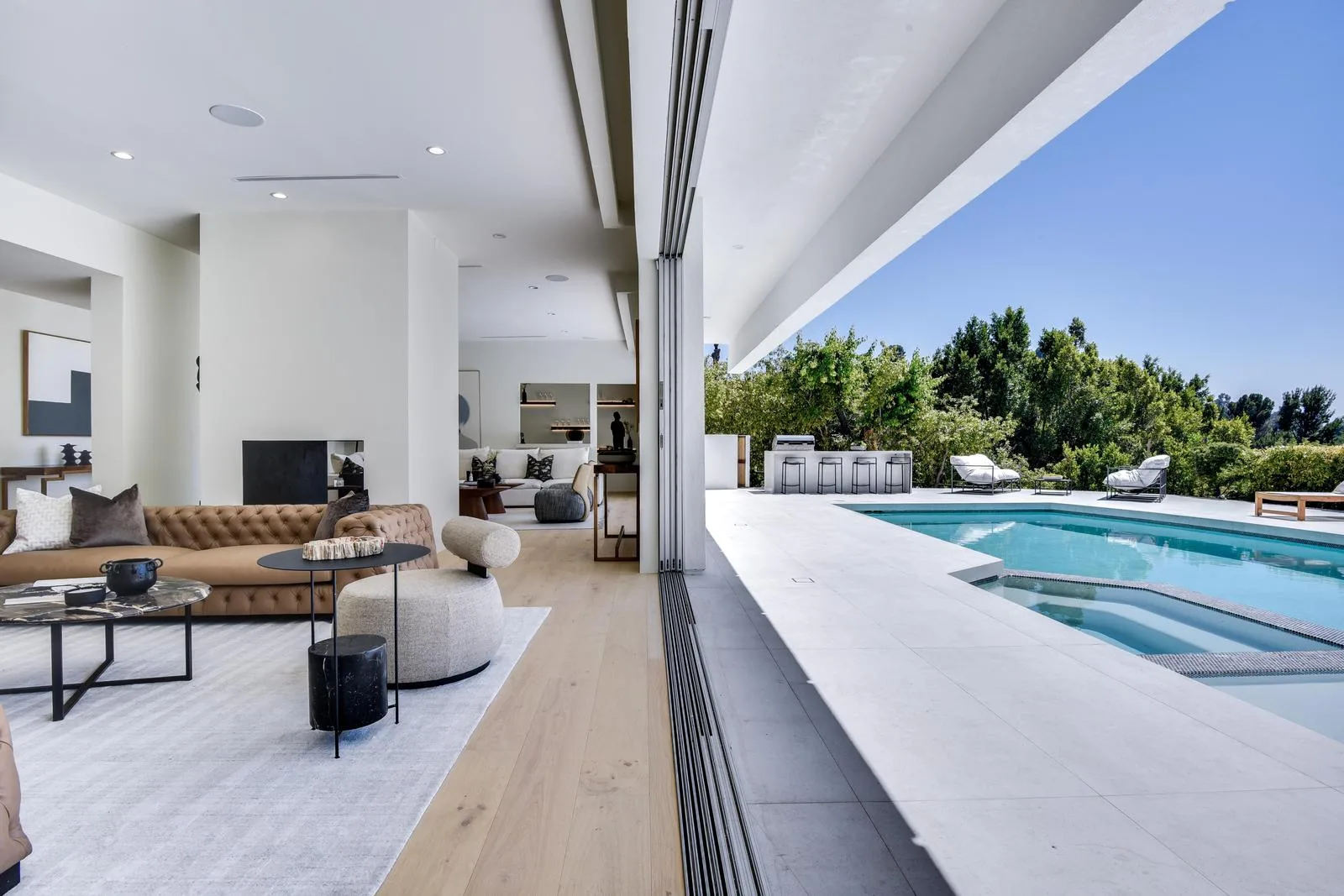 Living room with tufted tan sofa opening through retracted glass walls onto the pool terrace and spa