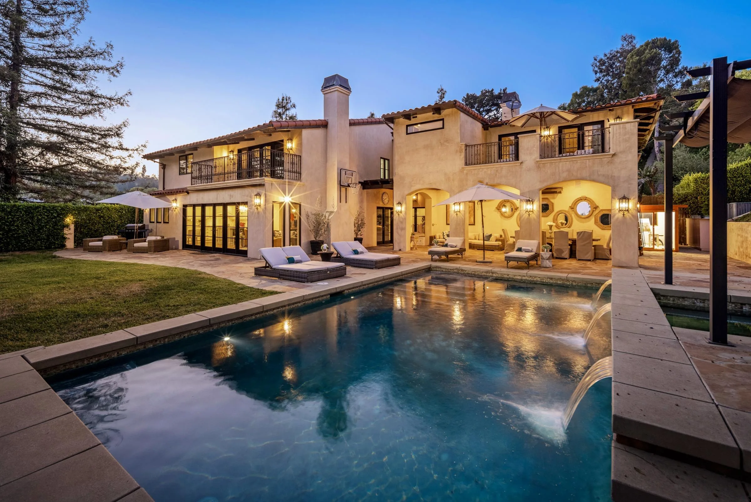 Pool and water spouts glowing at dusk below the lit Mediterranean facade of this Beverly Hills estate