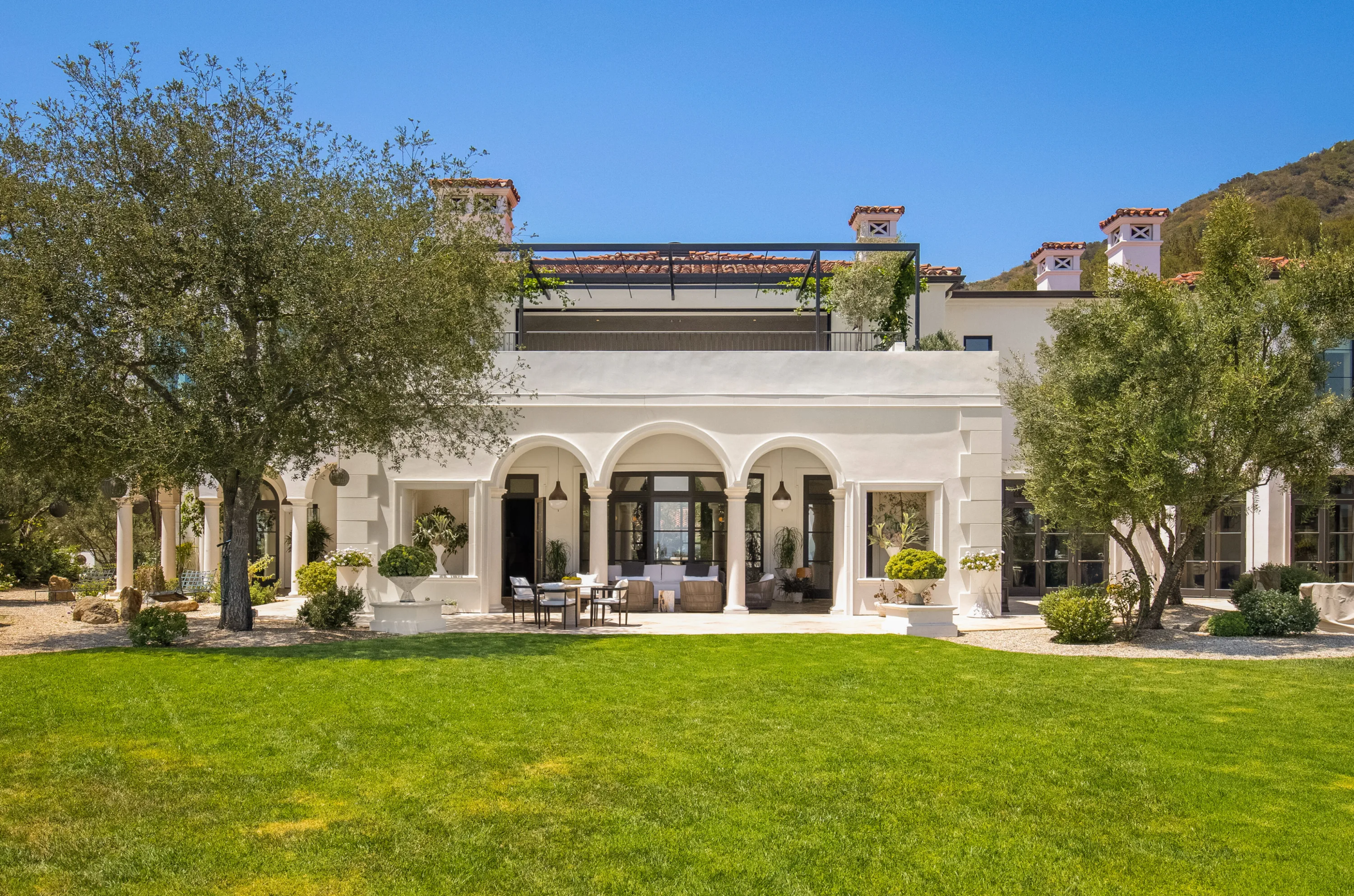 Rear facade seen across the lawn, arched loggia with seating below a vine-shaded roof terrace