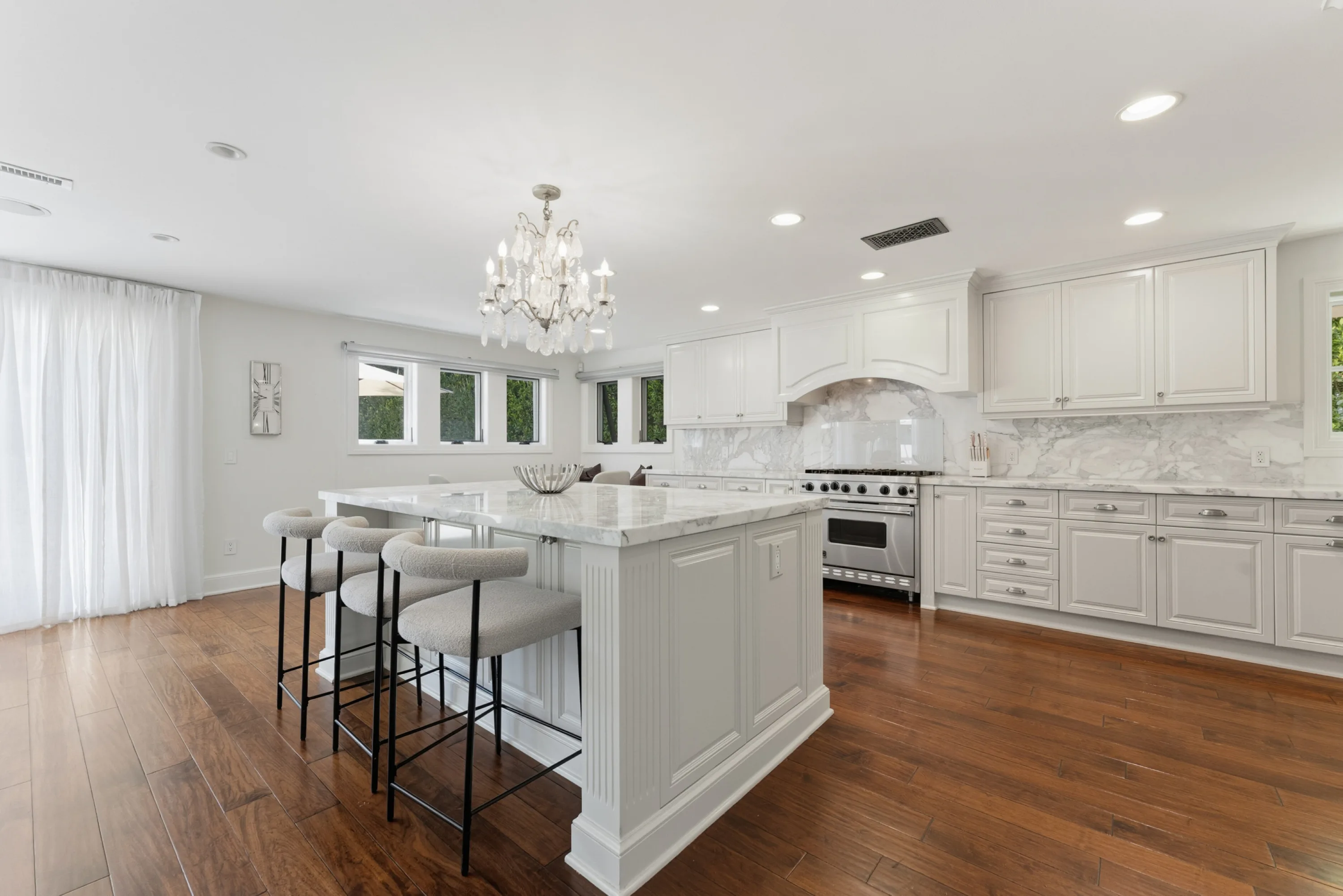 Chef's kitchen with marble island, three bar stools, range under a hooded alcove and chandelier