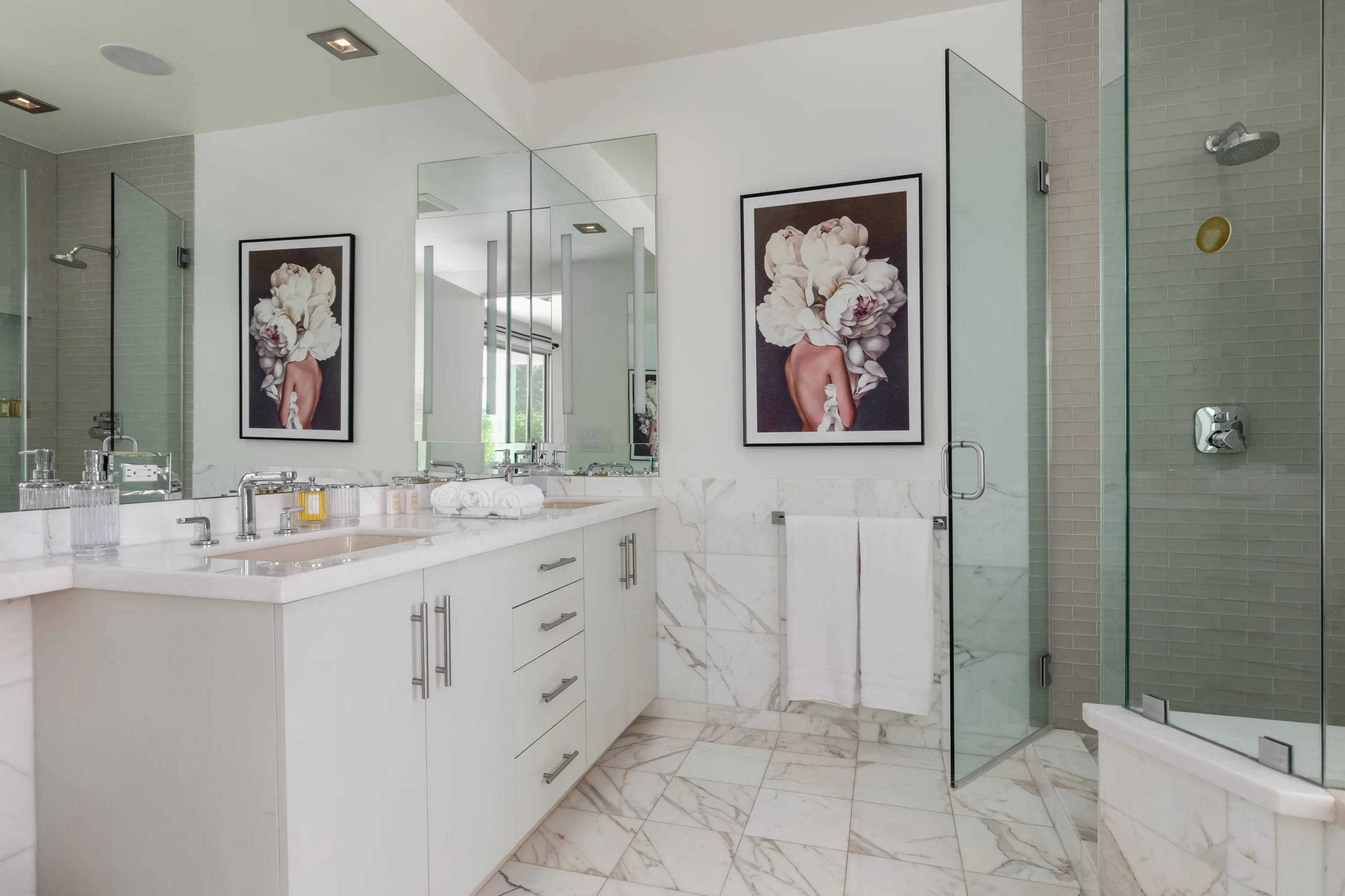 Marble-clad ensuite with double vanity, glass walk-in shower and framed floral-portrait prints