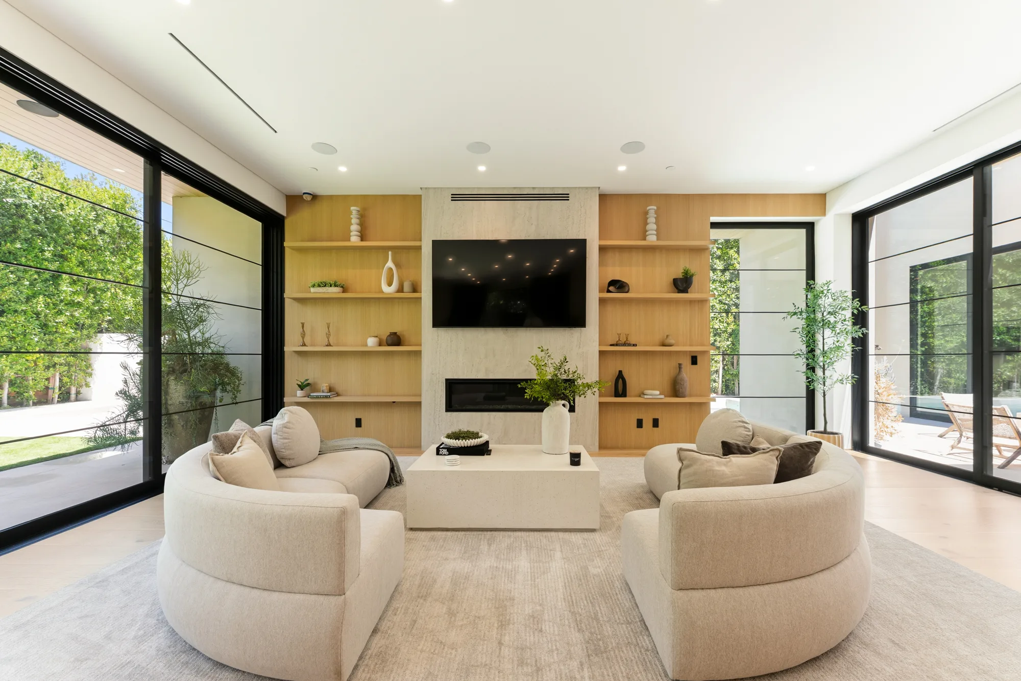 Twin curved sofas around a stone plinth table in the media lounge, framed by floor-to-ceiling windows