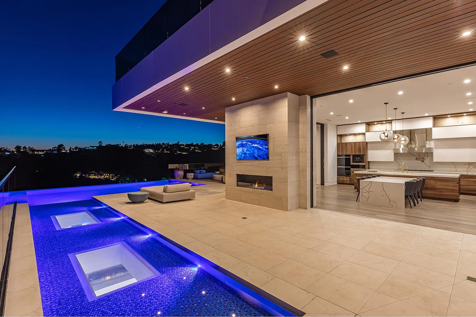 Poolside loggia after sunset with lit fireplace, outdoor screen and the kitchen open to the water's edge