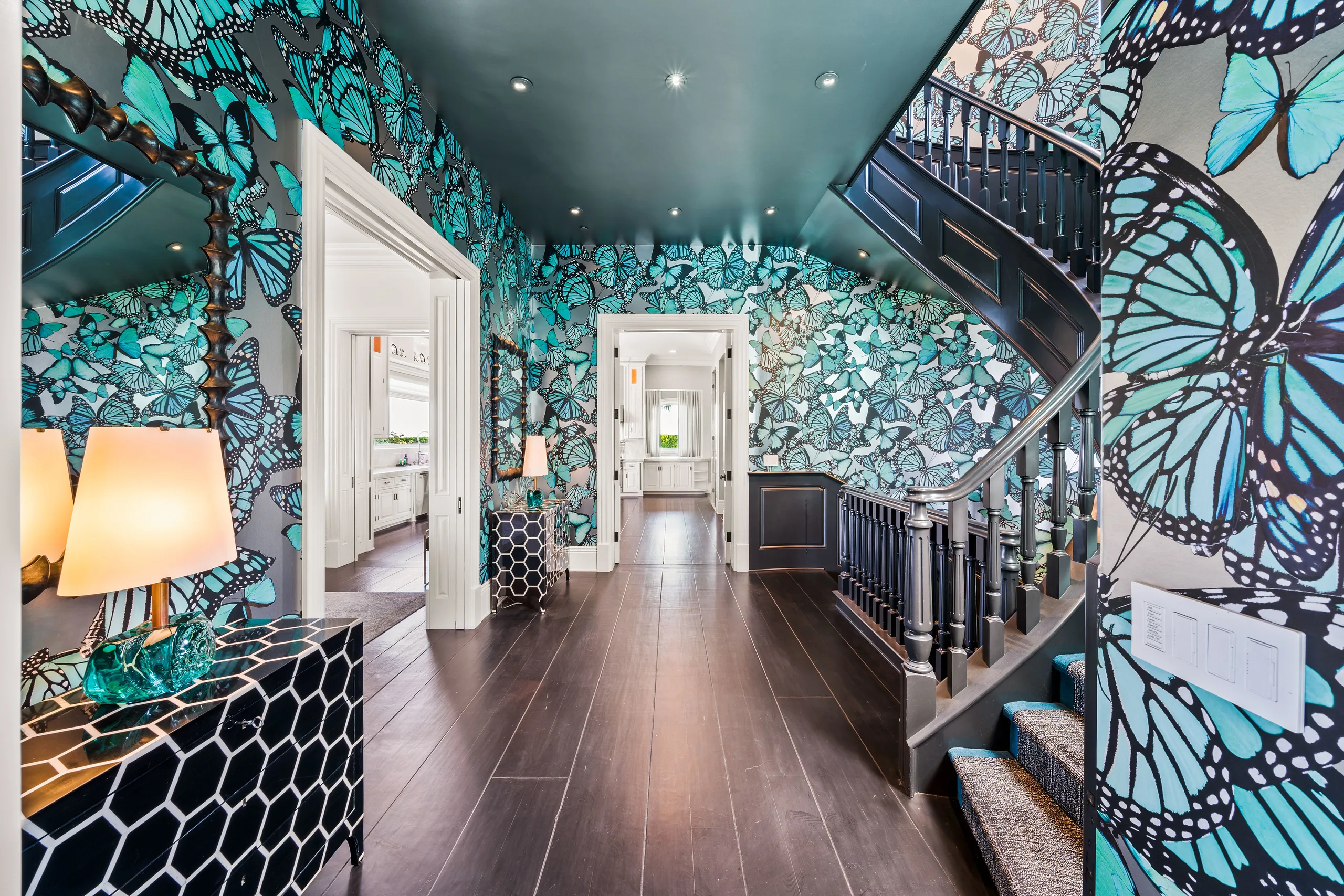 Butterfly-papered gallery hall in teal, curved dark staircase and lacquered honeycomb console