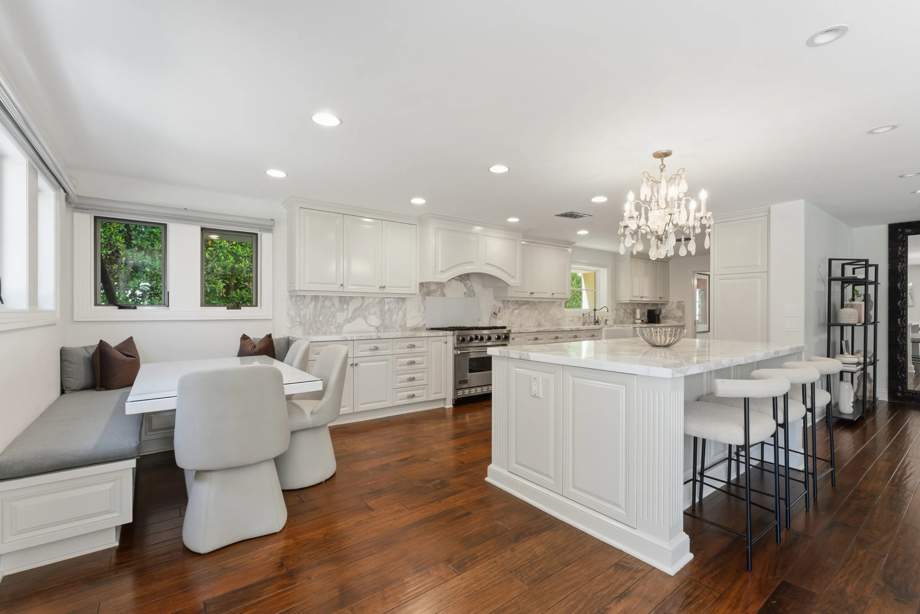 Breakfast banquette and marble-topped island in the white kitchen, windows onto the greenery