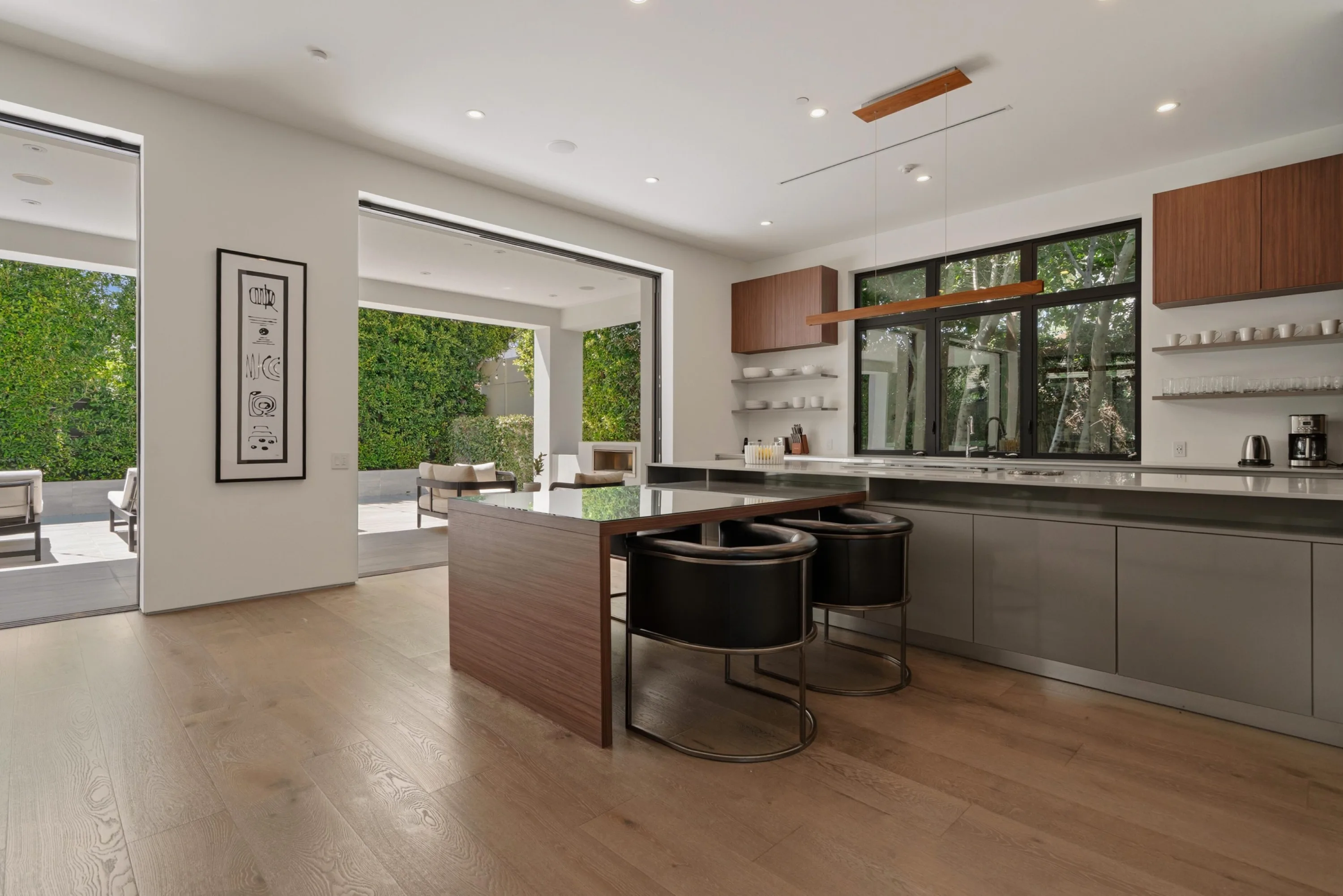 Chef's kitchen with breakfast bar stools, walnut cabinetry and glass doors folded back to the terrace