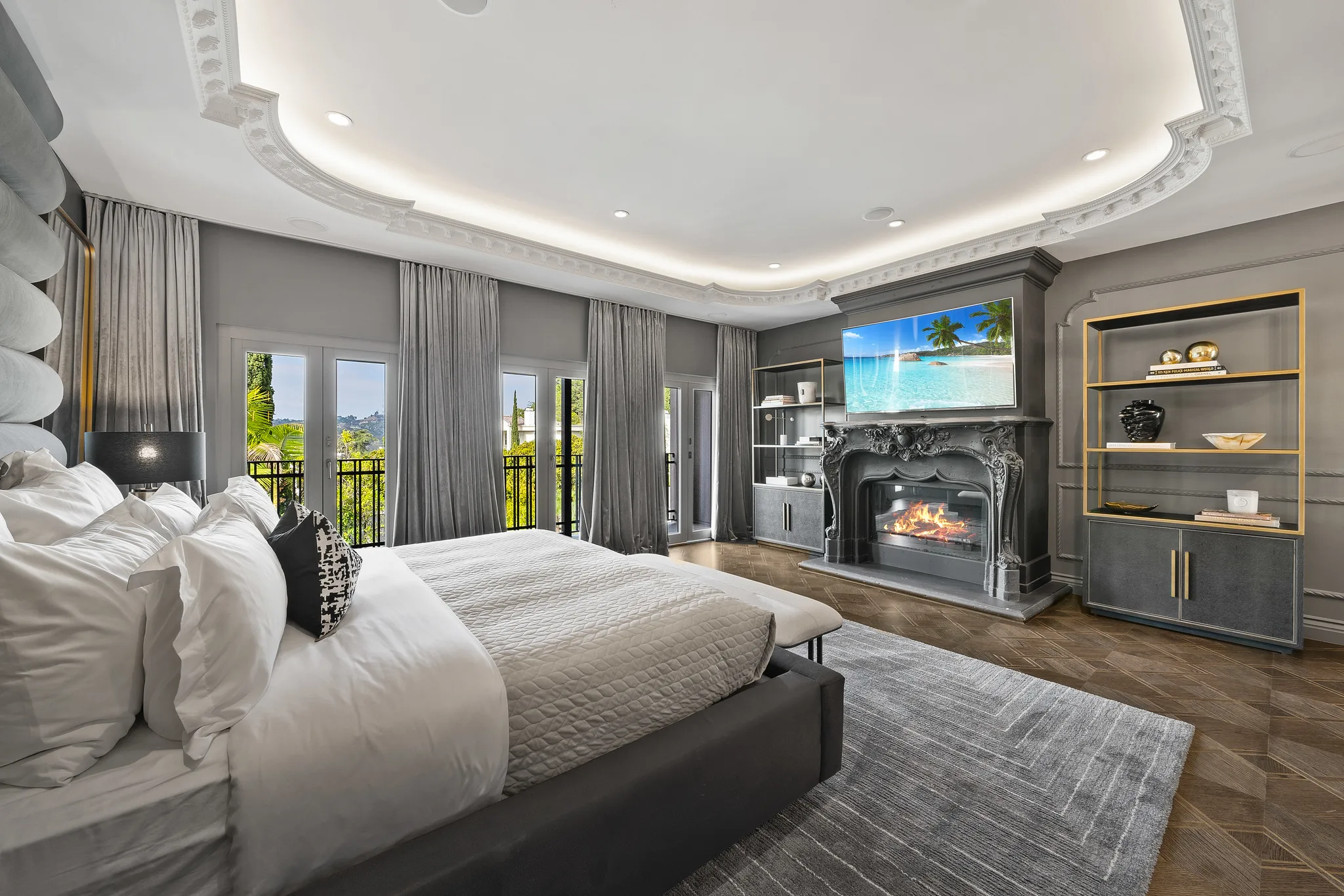 Primary bedroom fireplace lit beneath a mounted screen, treetops beyond the balcony doors