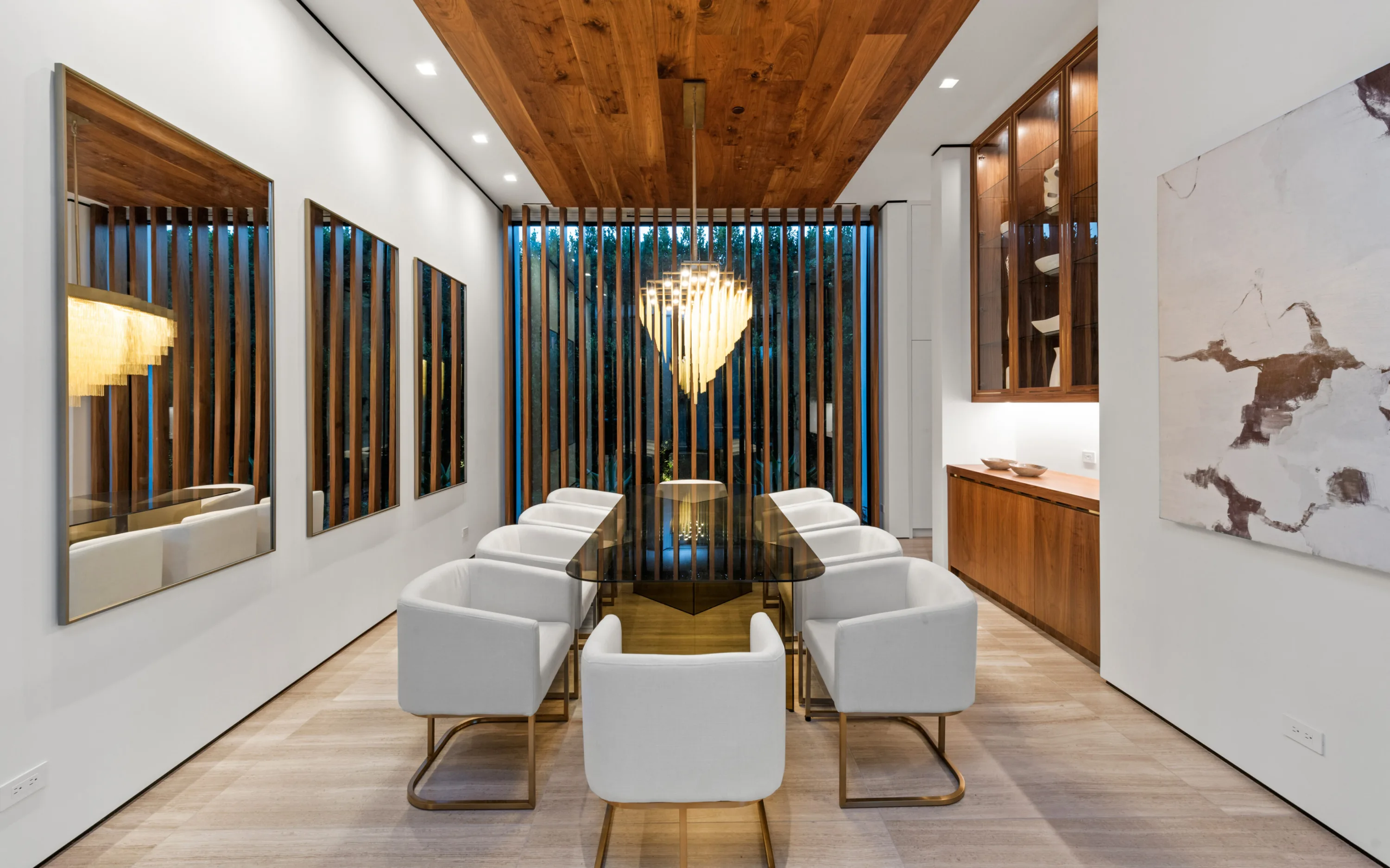 Formal dining room seating eight at a glass table below a fringed brass chandelier and slatted screen