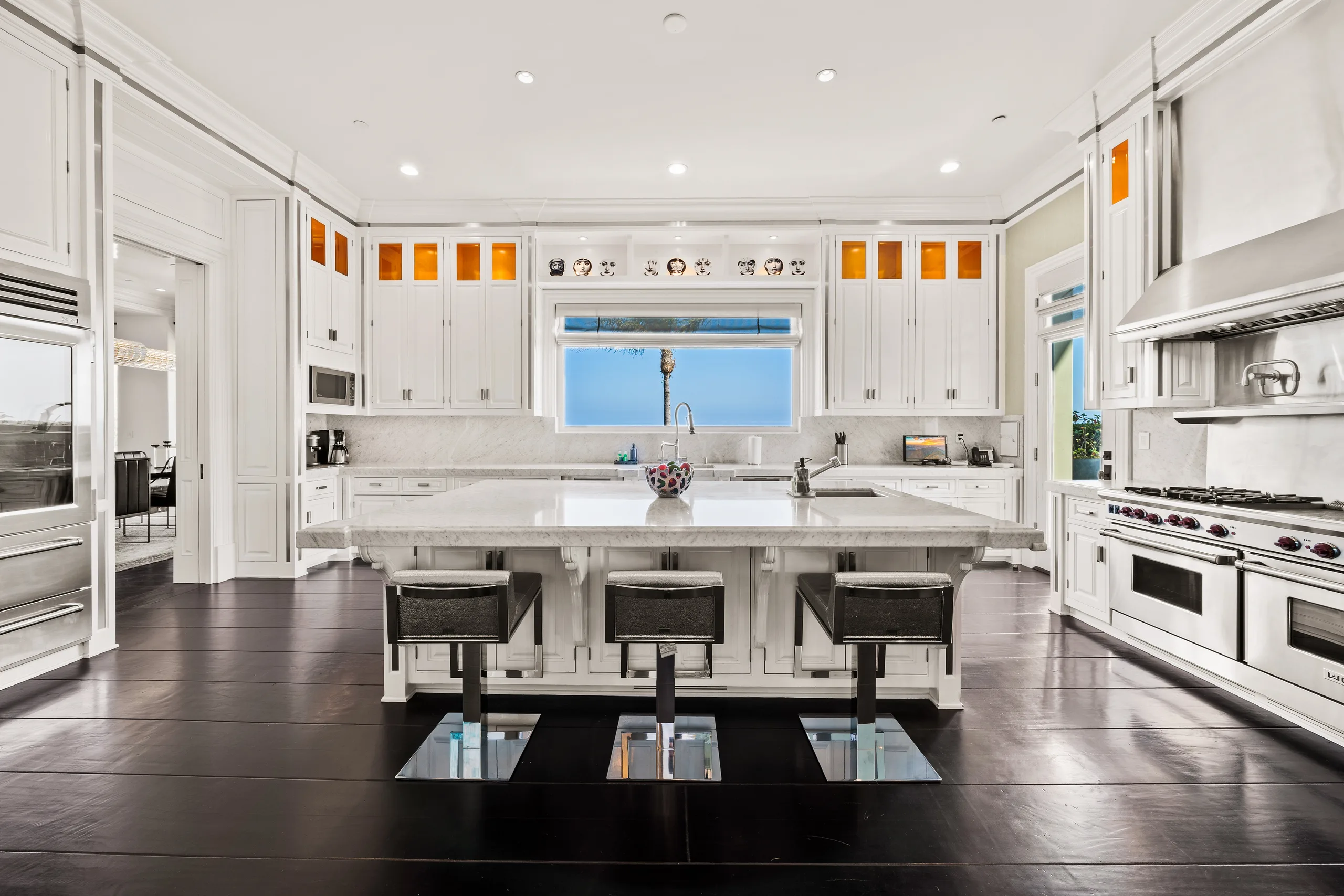 Chef's kitchen with marble island, three barstools, pro range and a palm-framed window