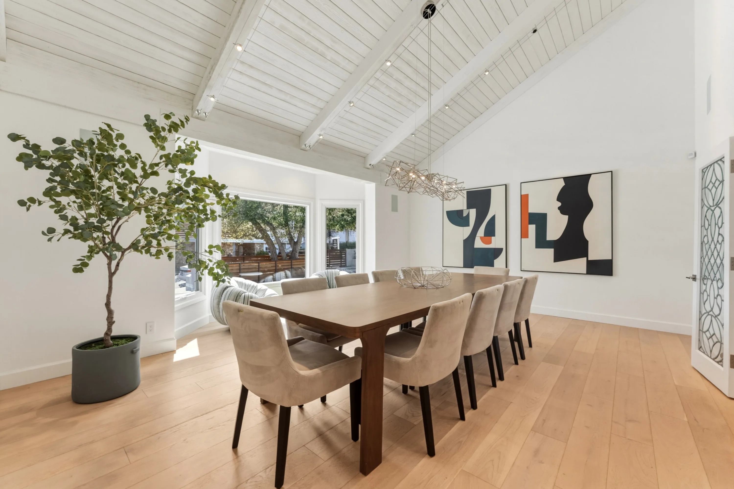 Formal dining room seating ten beneath a sculptural chandelier and whitewashed vaulted ceiling