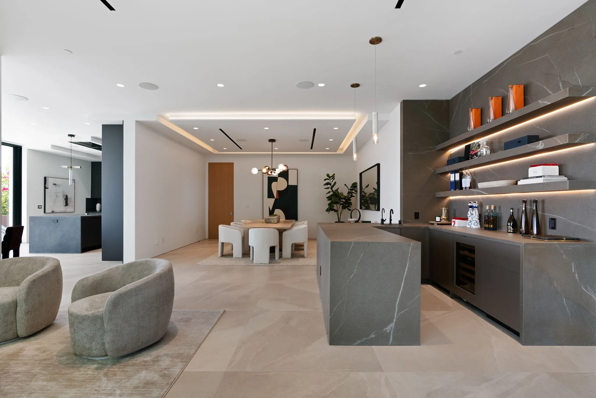 Stone-topped wet bar with backlit shelving, beside the dining table and sitting area