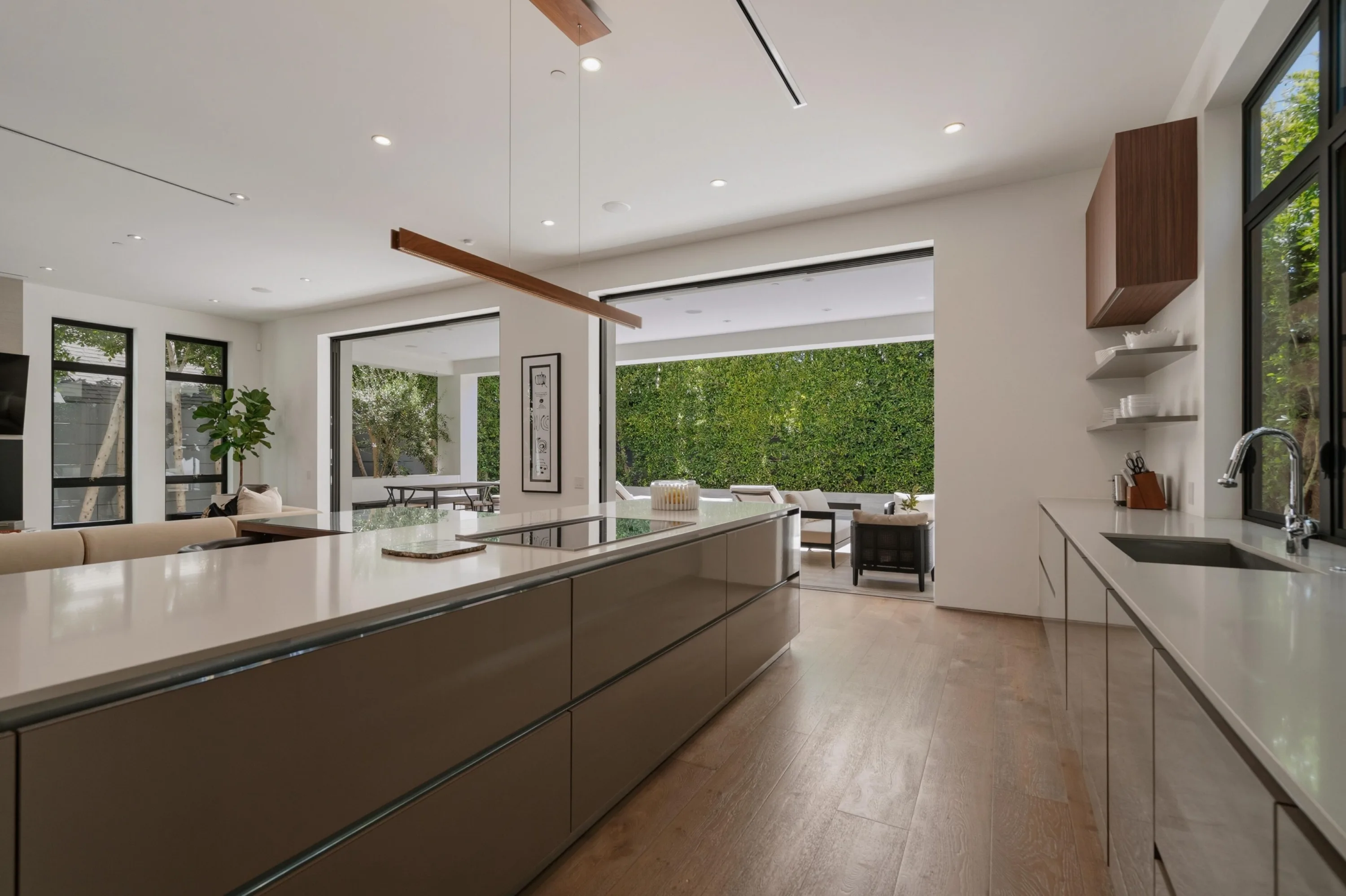 Long kitchen run with prep sink and induction island facing the open-air lounge and hedge wall