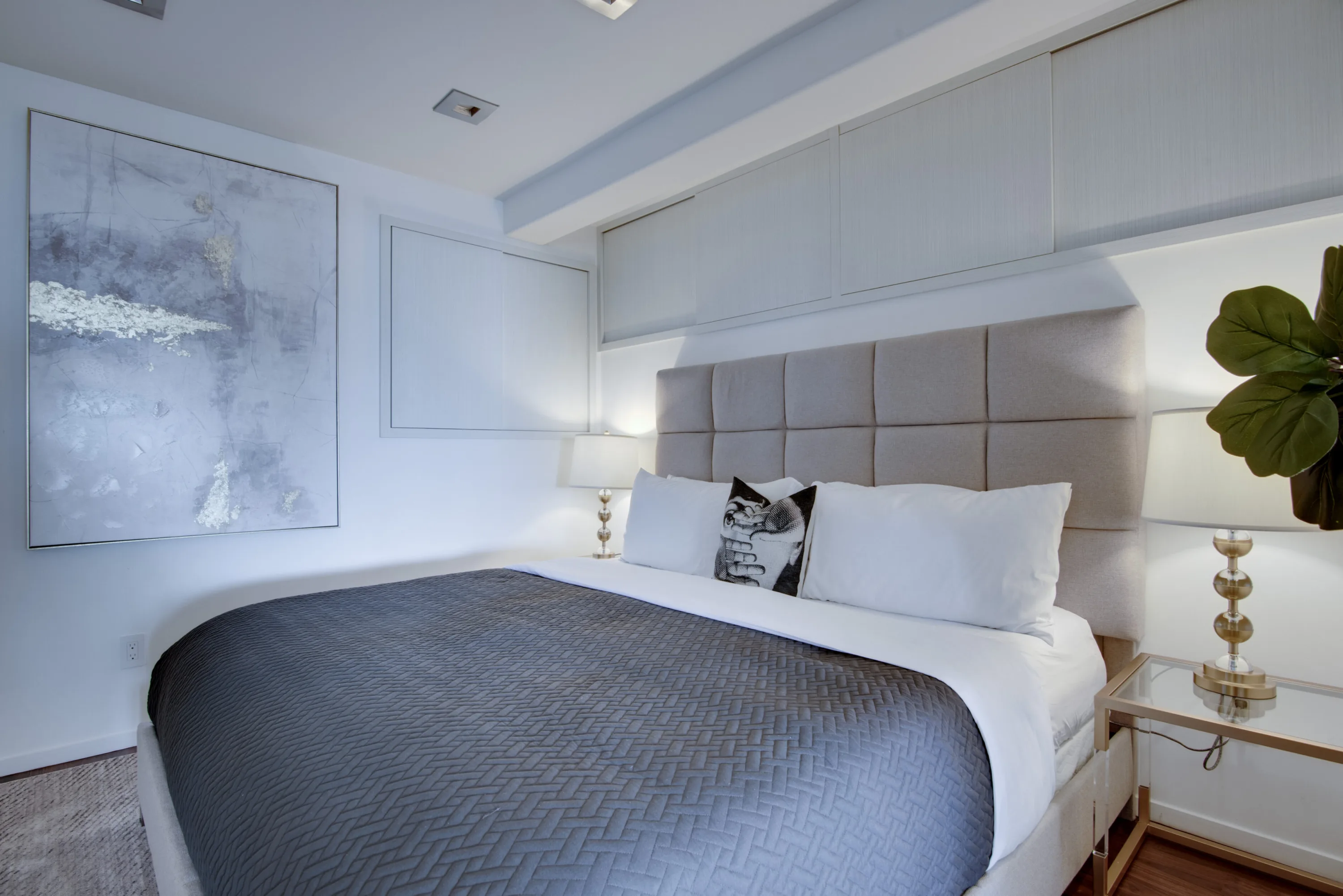 Lower-level bedroom in soft greys, tufted headboard flanked by lamps and a large abstract canvas