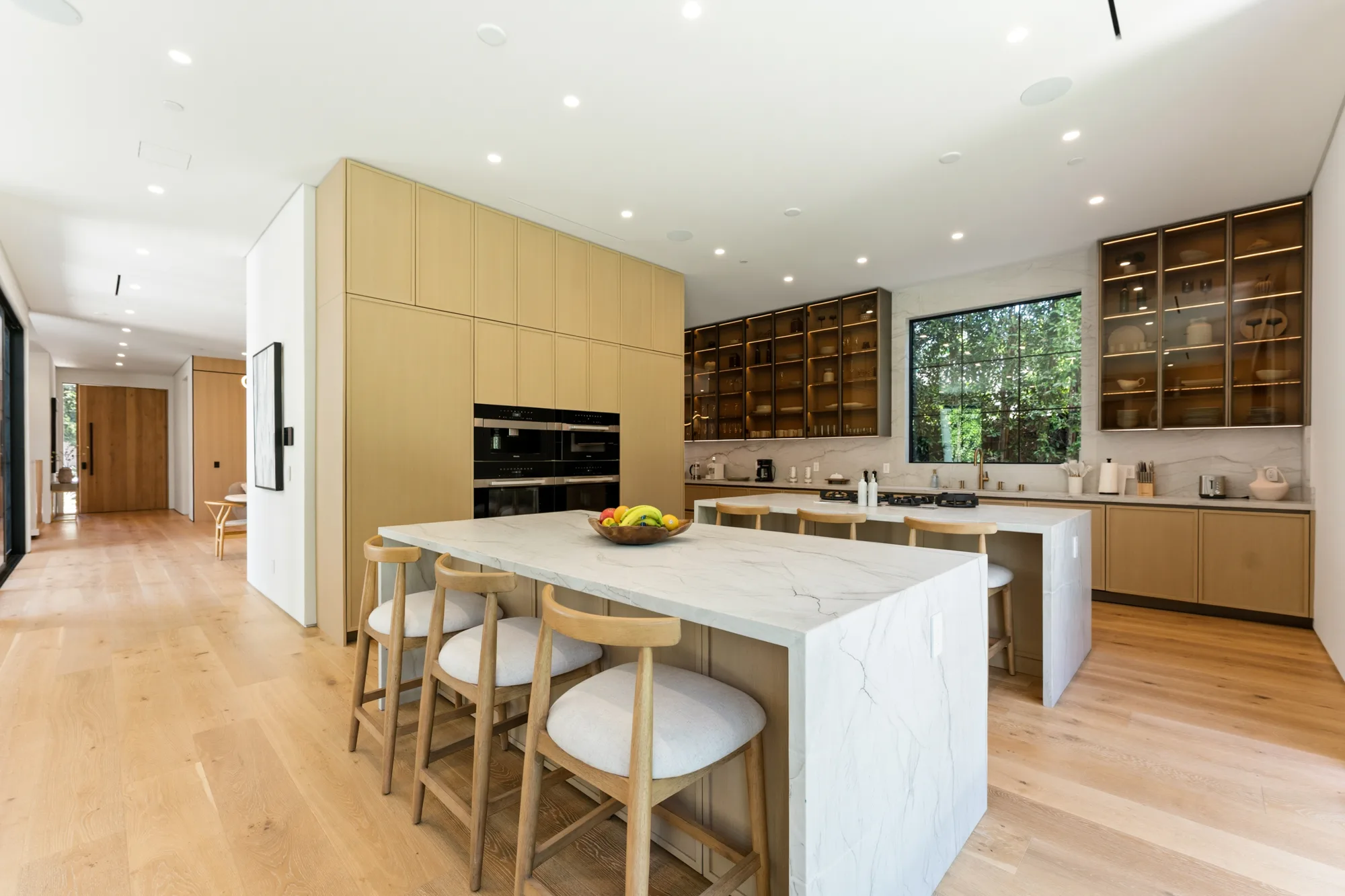 Chef's kitchen with veined marble waterfall island, oak cabinetry and backlit glass-front cupboards