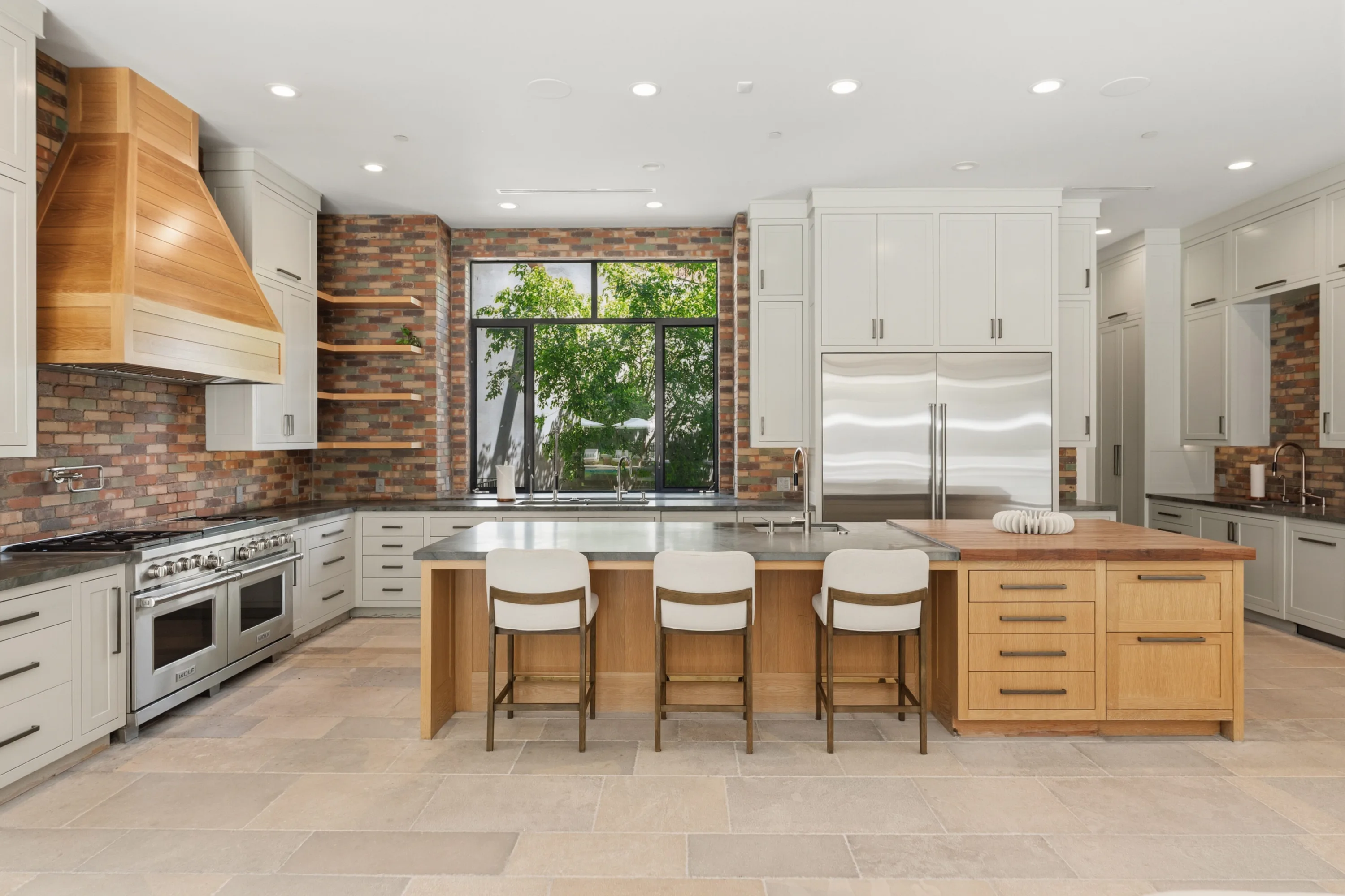 Chef's kitchen with double range, brick backsplash, twin islands and three stools under a garden window