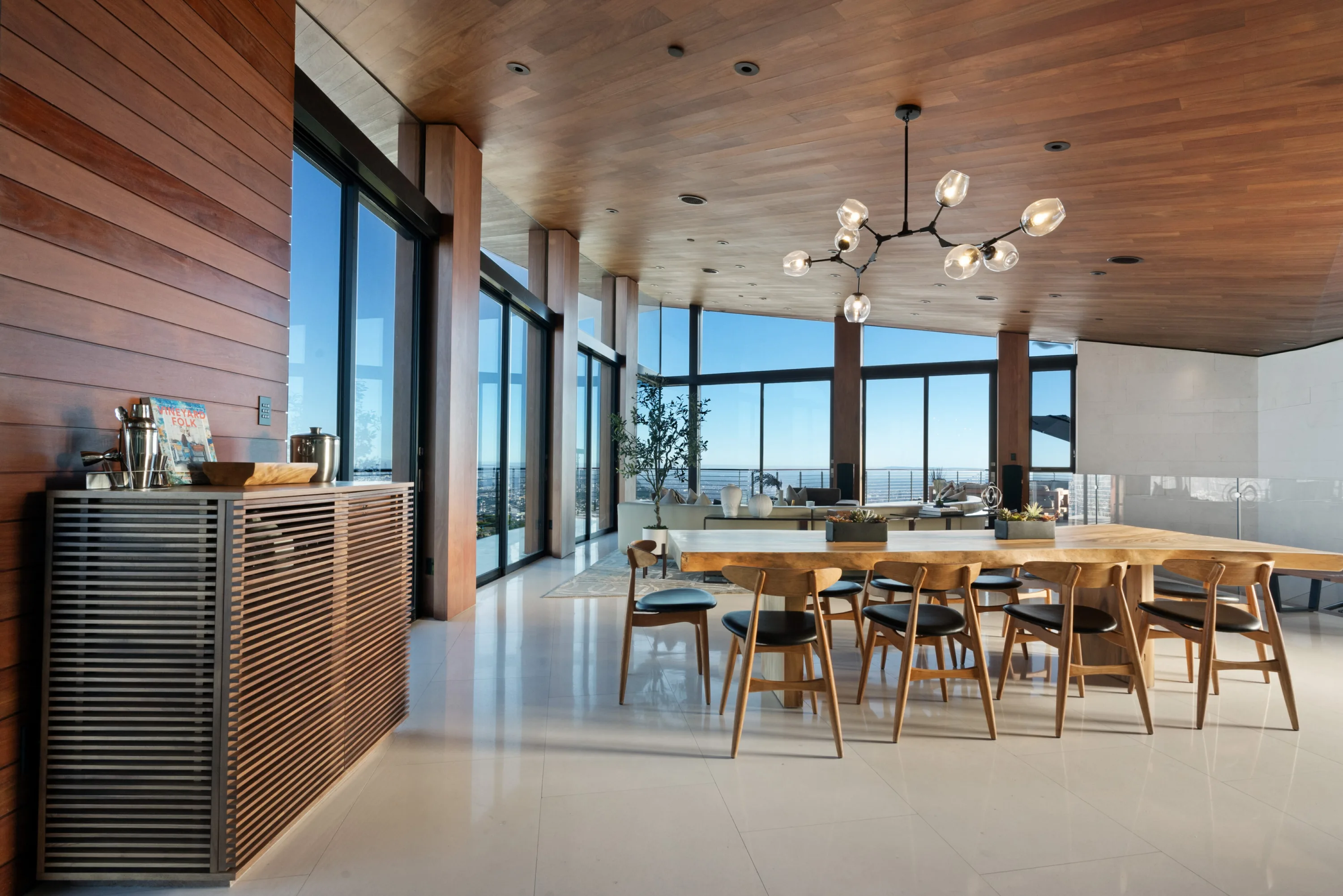 Dining area along the cedar-clad wall, slatted bar cabinet in the foreground and lounge beyond the glass