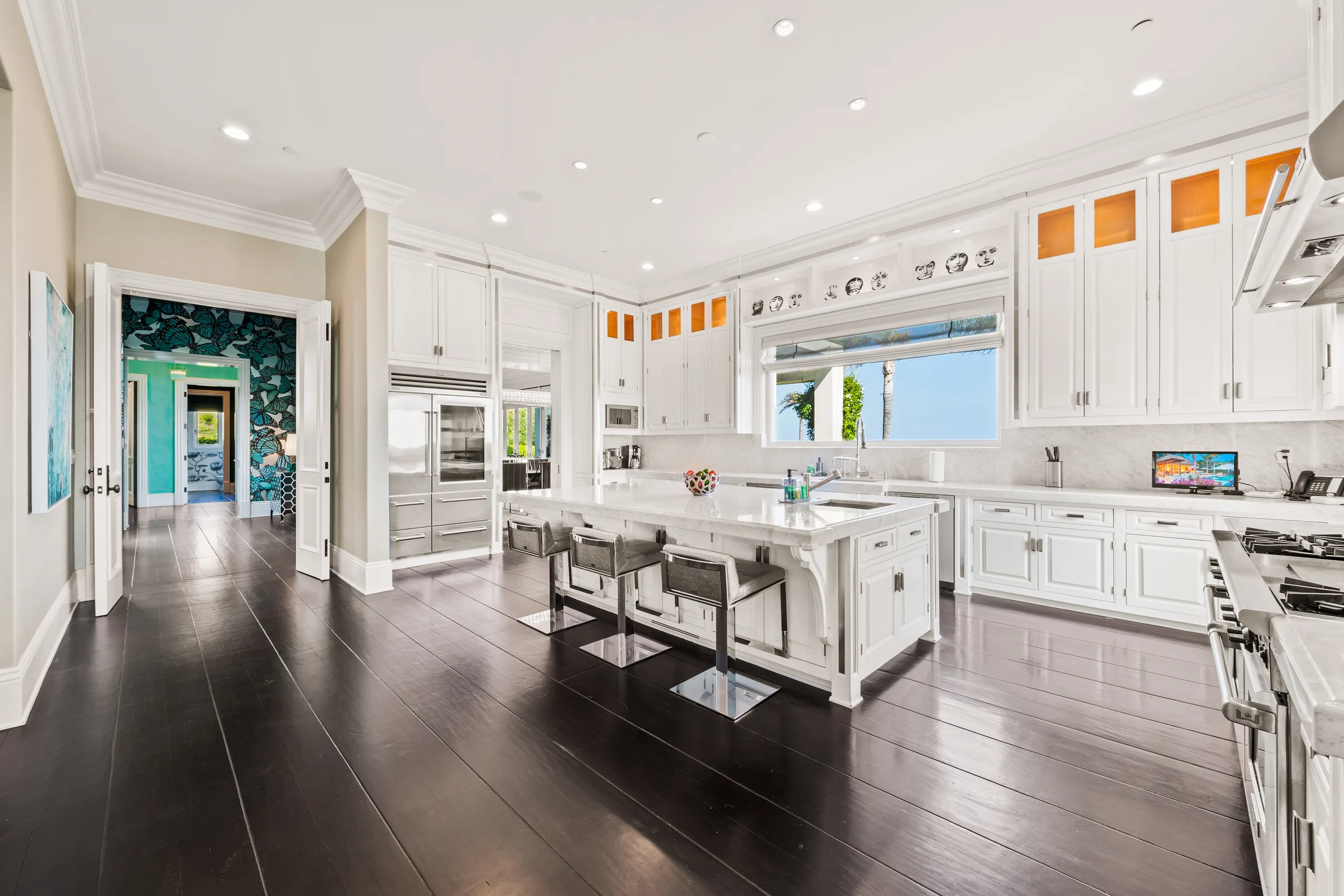 Wider kitchen view down ebony plank floors, teal butterfly hallway visible through open doors