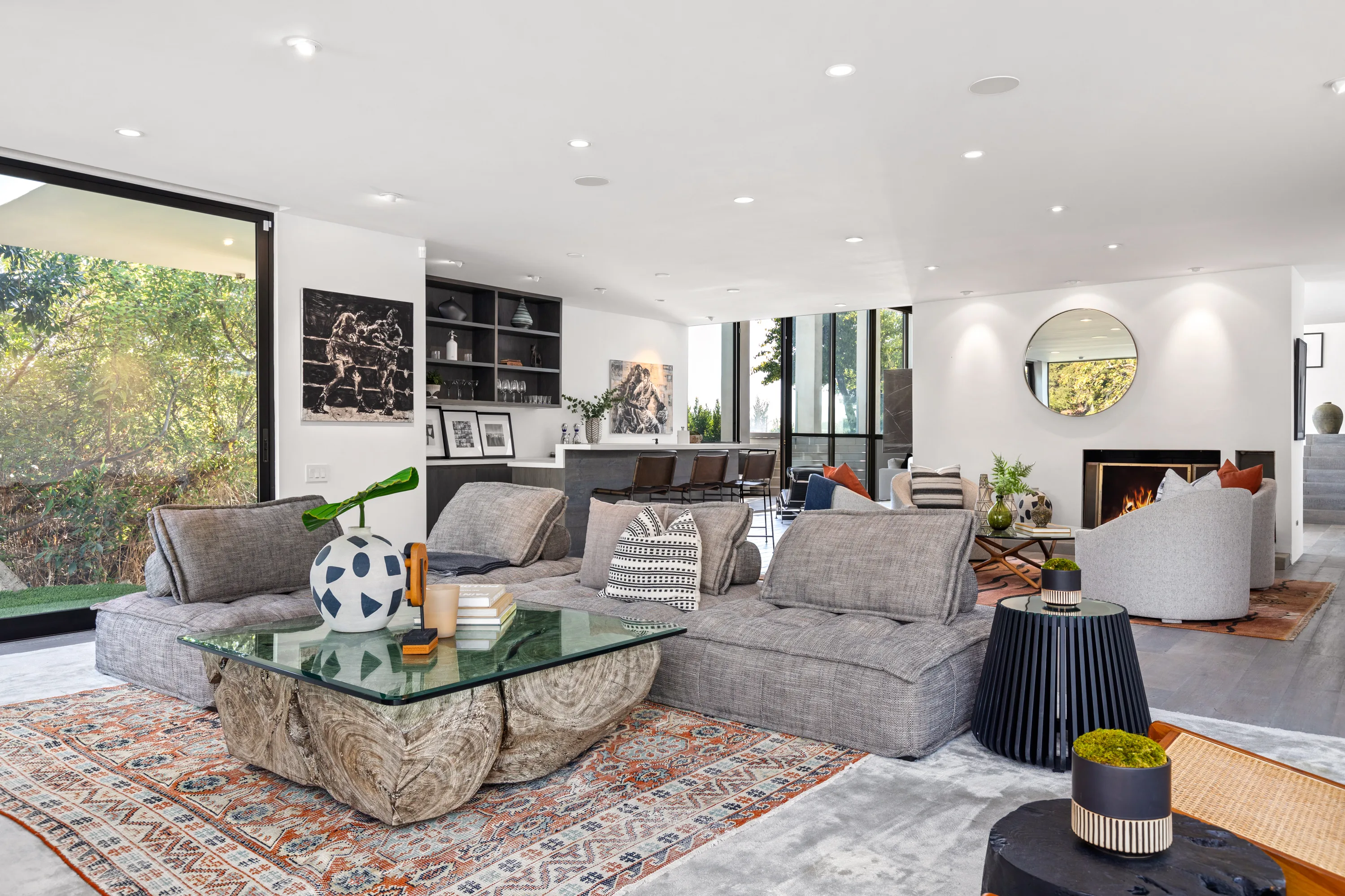 Deep modular sofa on layered rugs, framed by glass walls onto the garden and the bar beyond