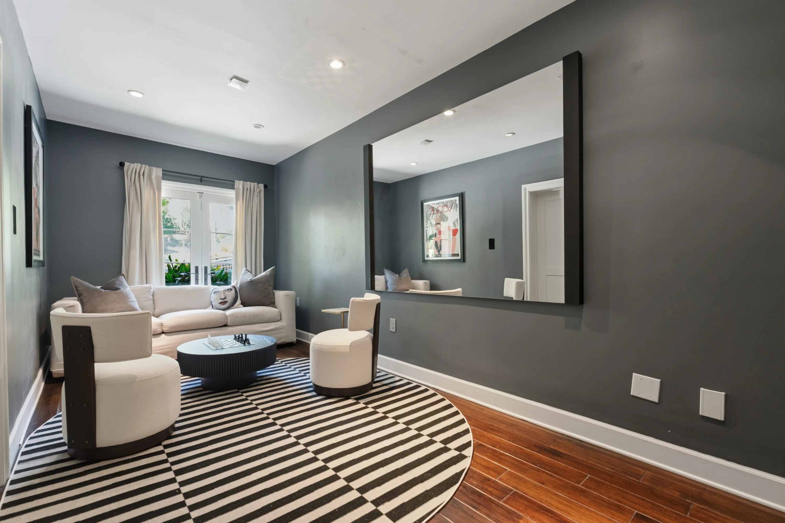 Charcoal-walled sitting room with striped round rug, swivel chairs and oversized wall mirror