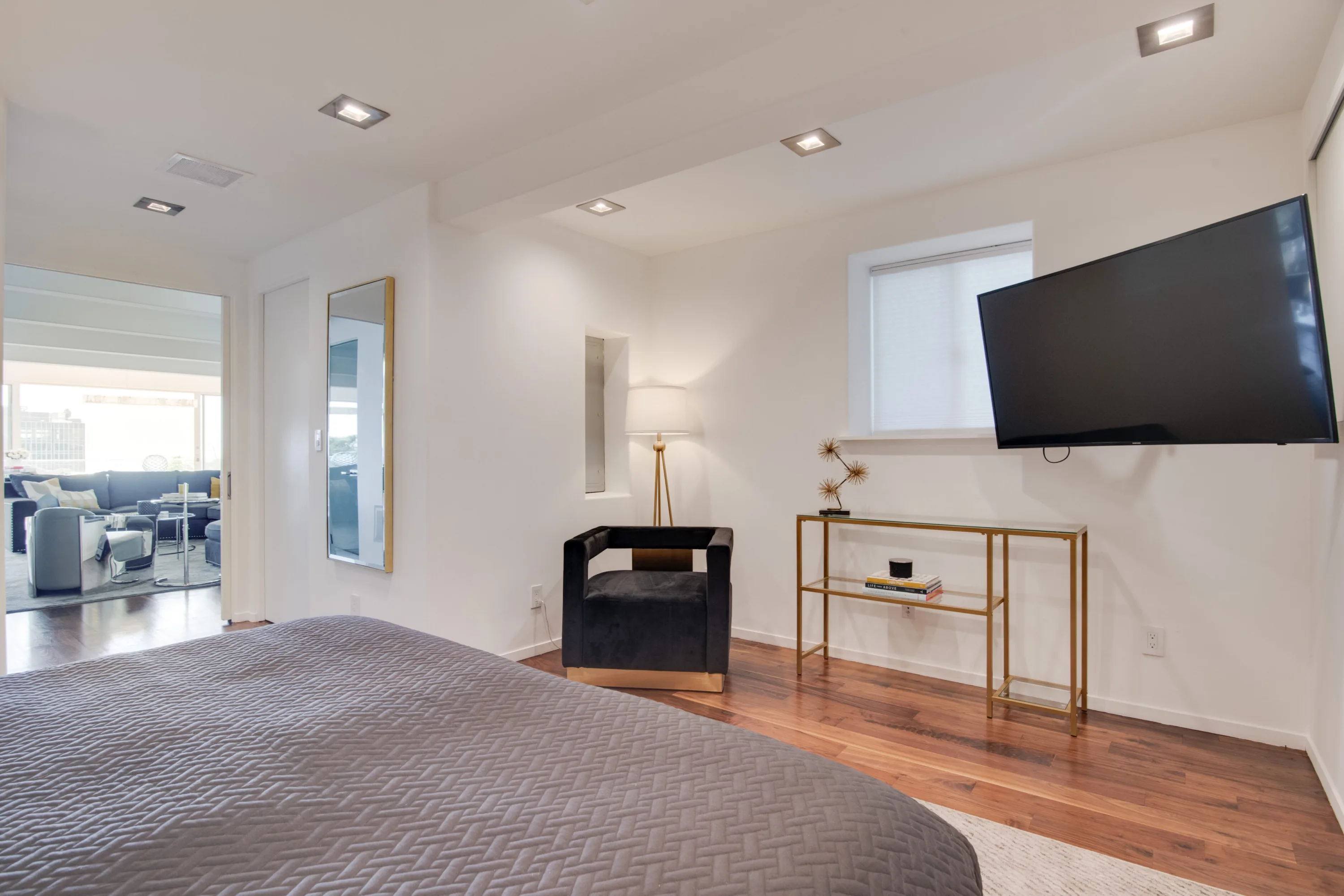 Bedroom corner with velvet armchair, brass console and mounted TV, open to the adjoining lounge