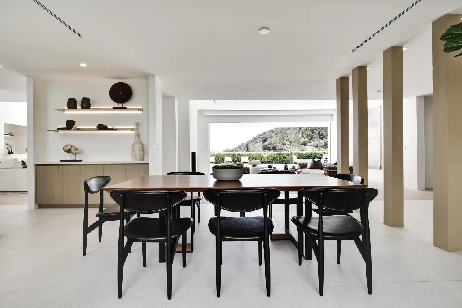 Walnut dining table for eight with black chairs, lined up with the hillside view through open doors