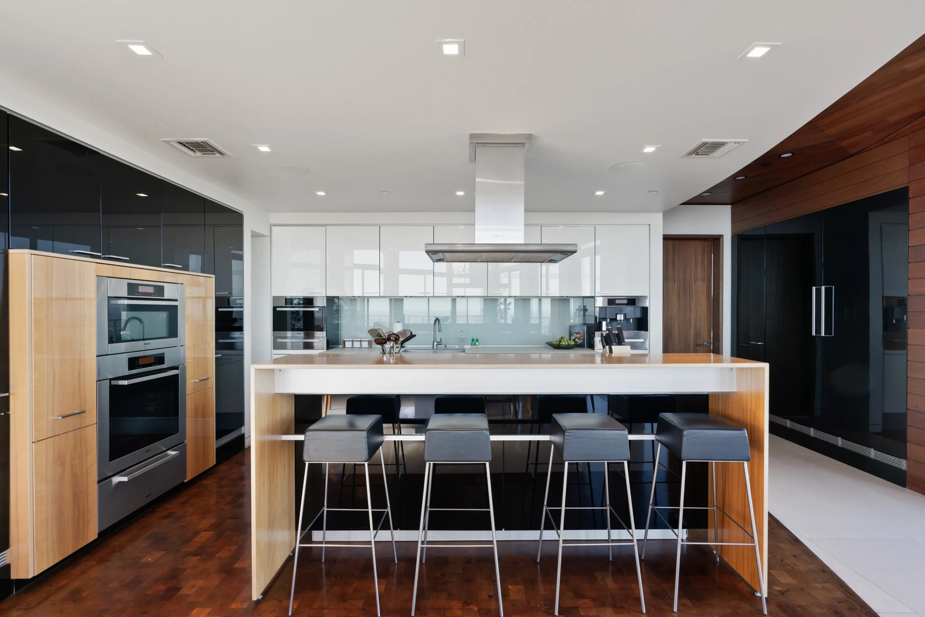 Chef's kitchen with white island, four leather bar stools, double wall ovens and mirrored glass backsplash
