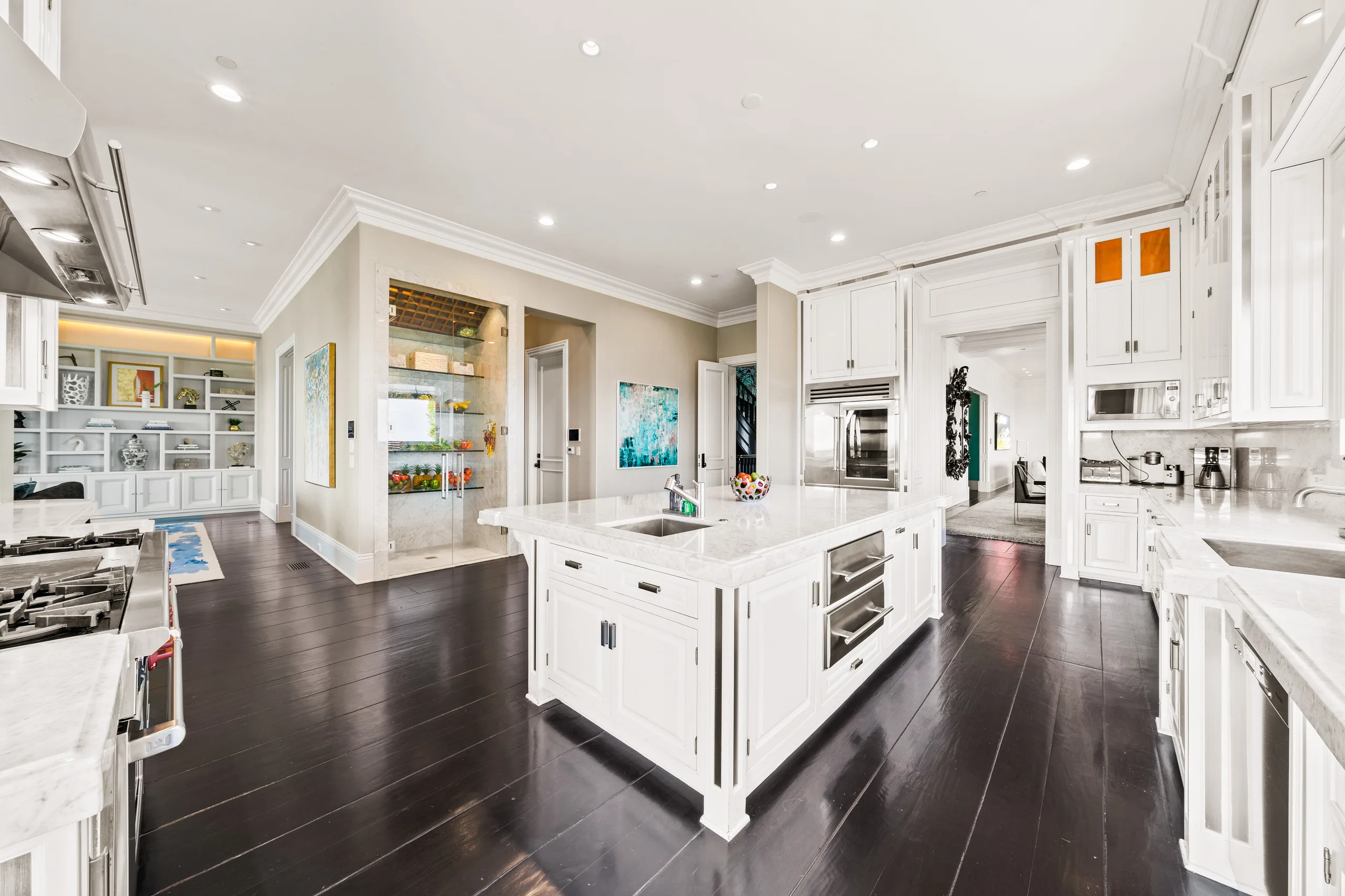 Second prep island with sink and warming drawers, glass-walled pantry and built-in shelving beyond