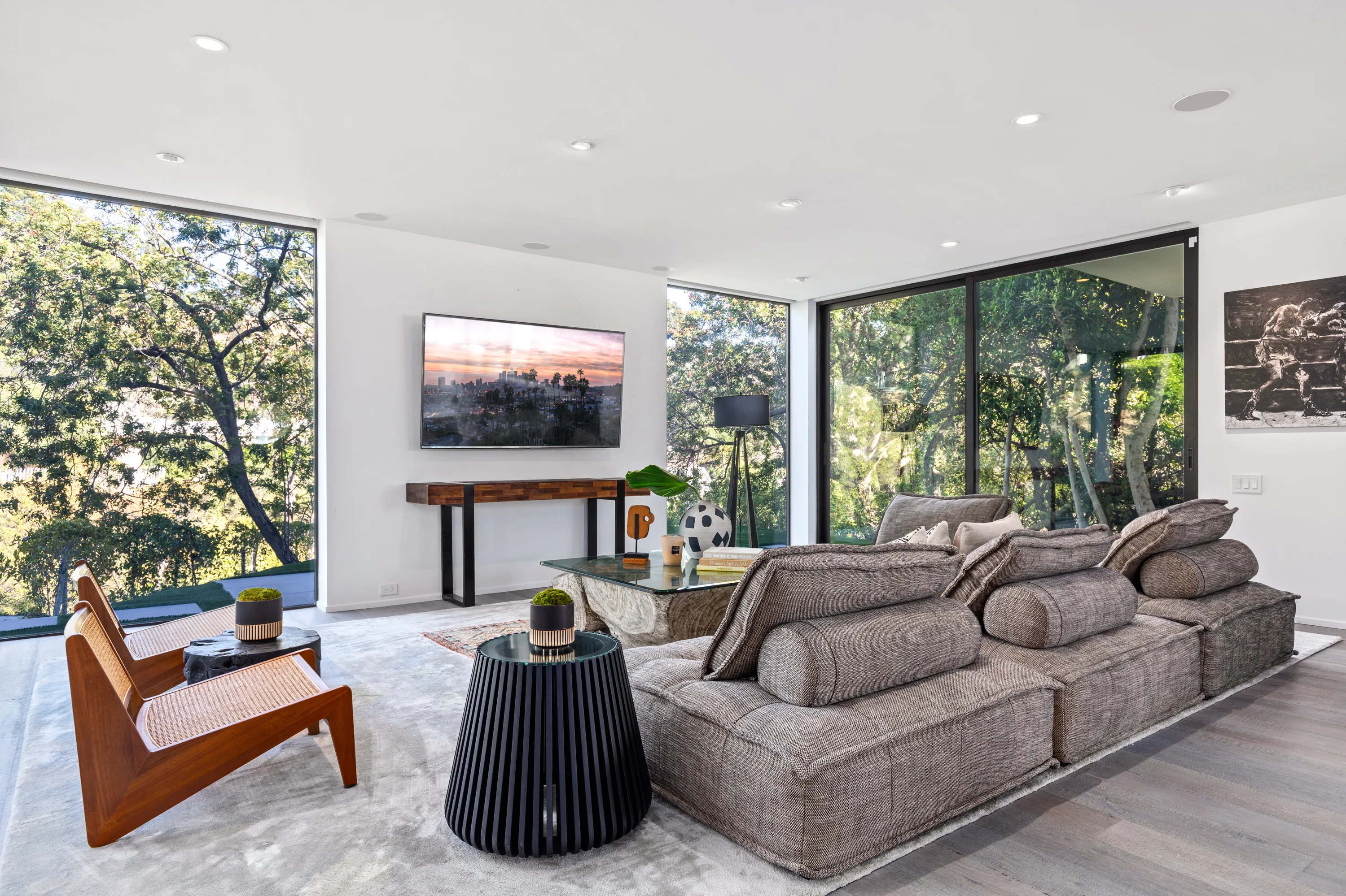 Media lounge with oversized sectional, wall-mounted screen and treetop views through corner glass