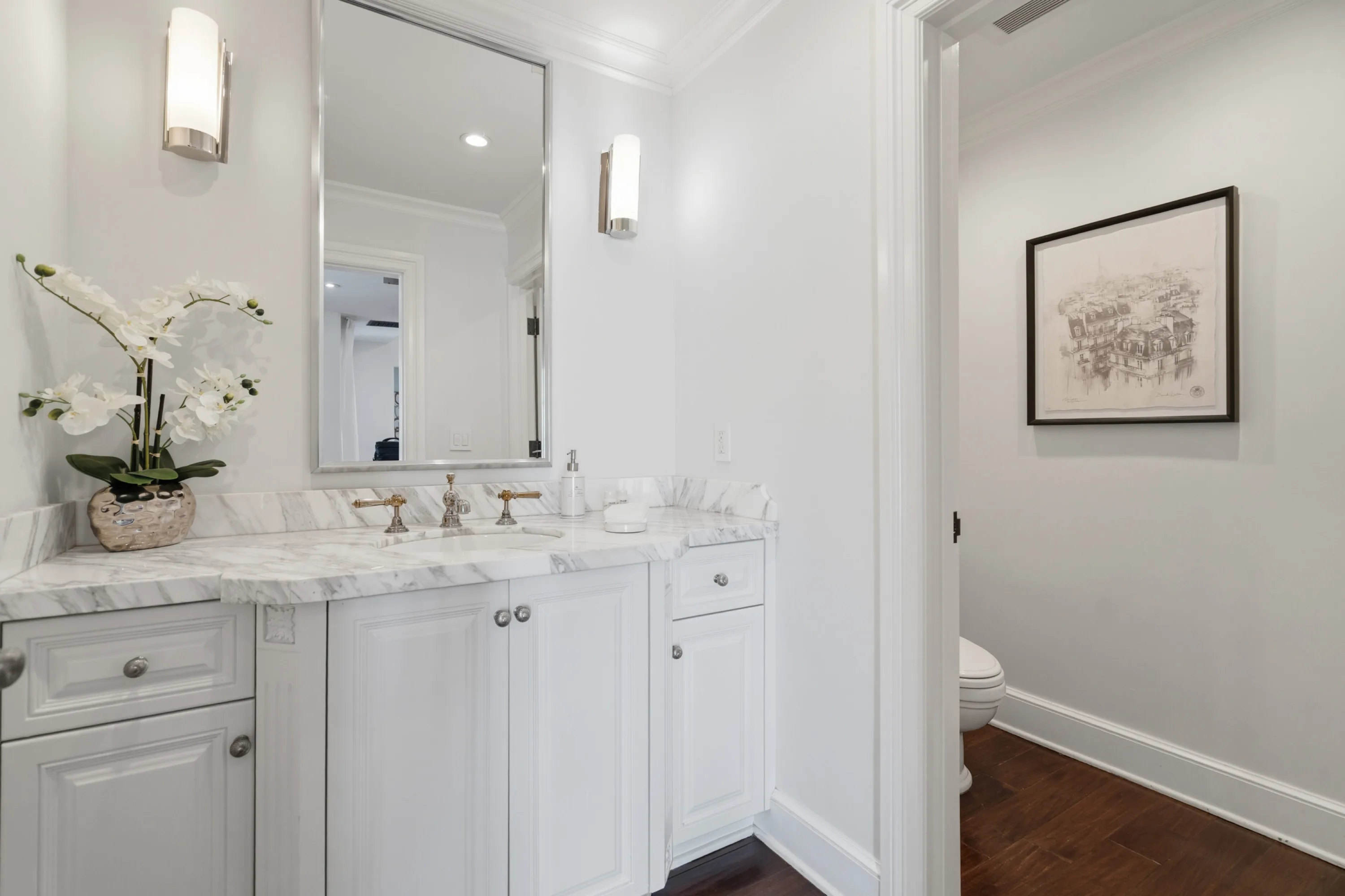 Powder room with marble vanity, orchid and framed sketch in the adjoining alcove