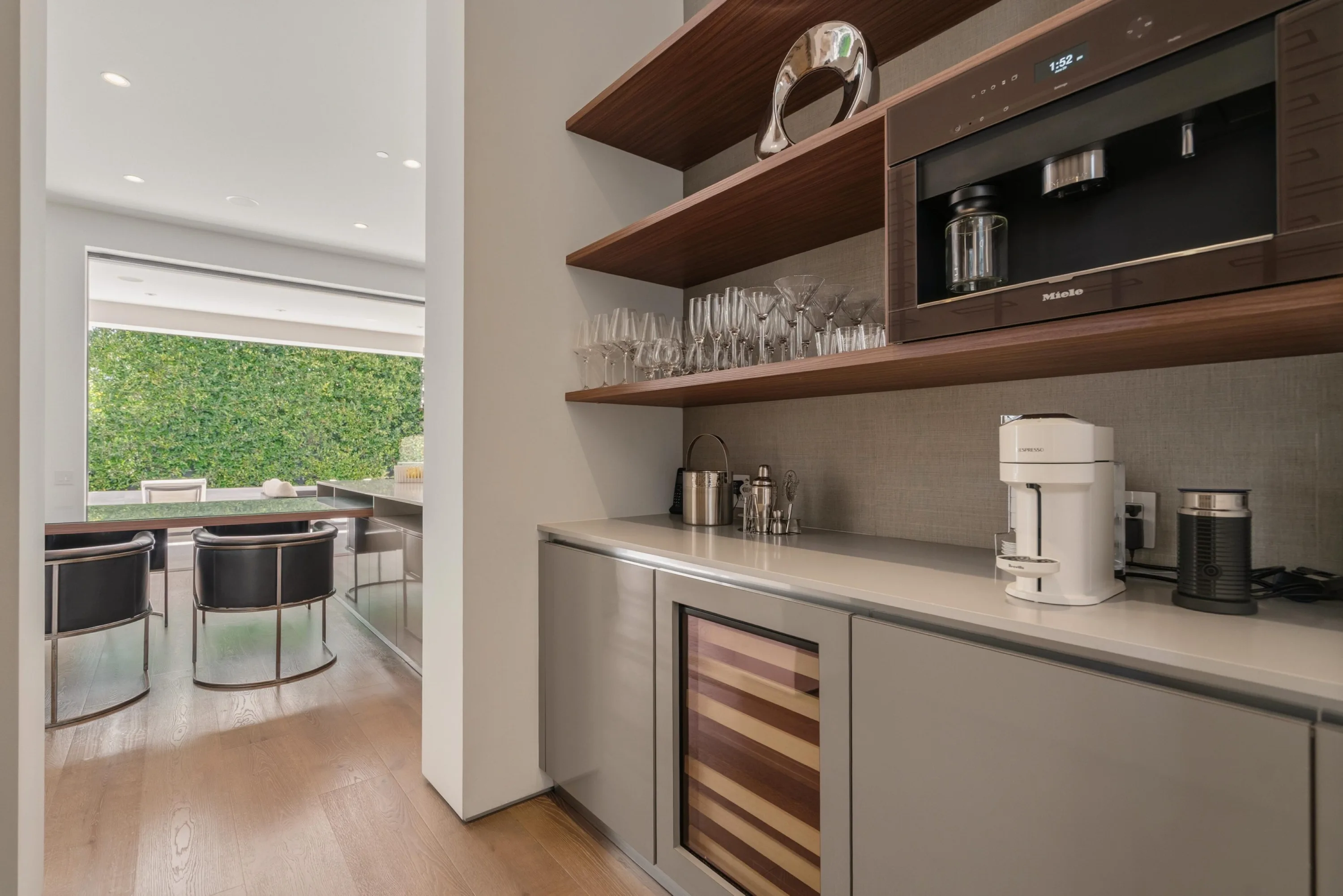 Butler's pantry with built-in Miele coffee system, wine fridge and stemware on walnut shelves