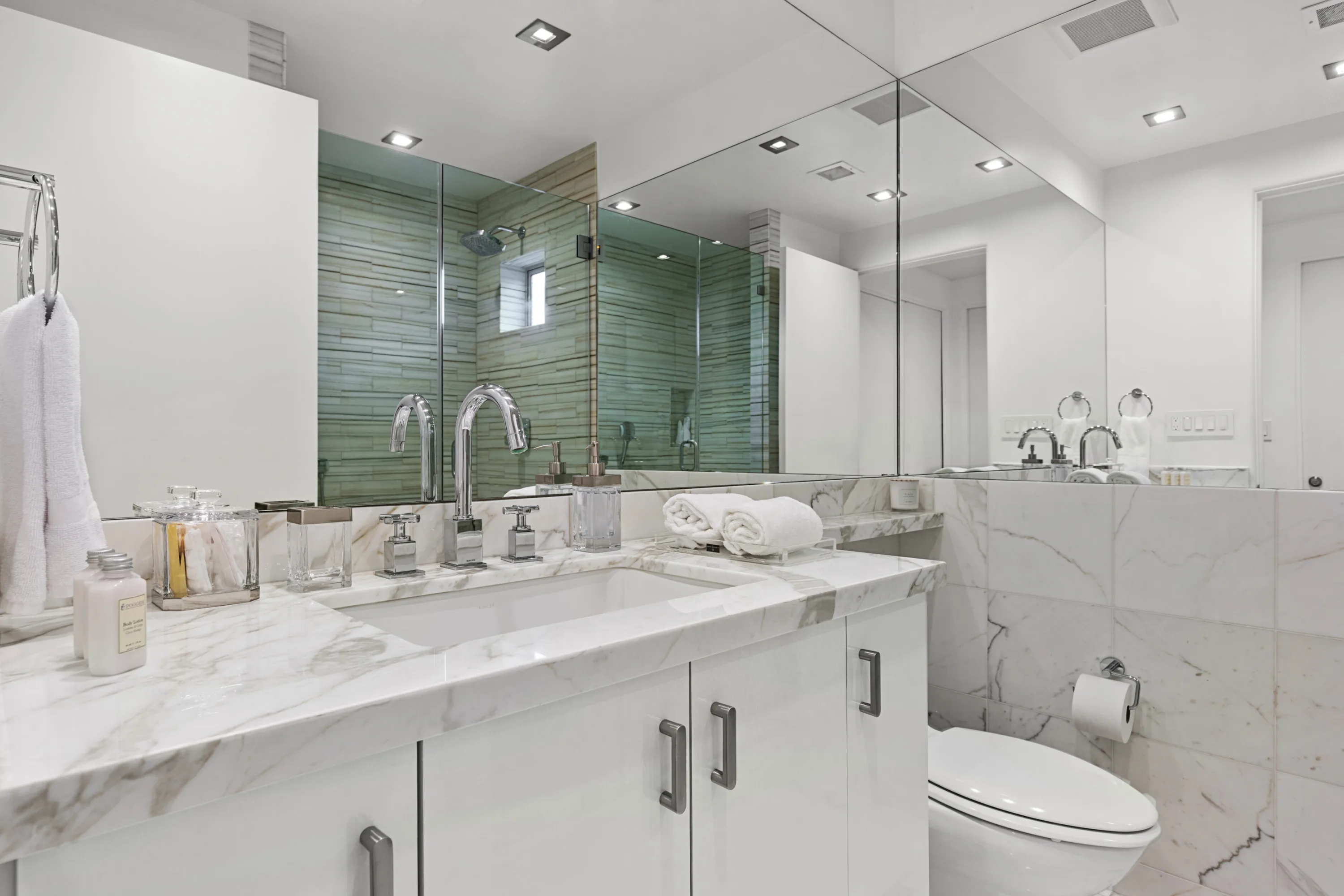 Guest bathroom with marble vanity, rolled towels and a green glass-tiled rain shower