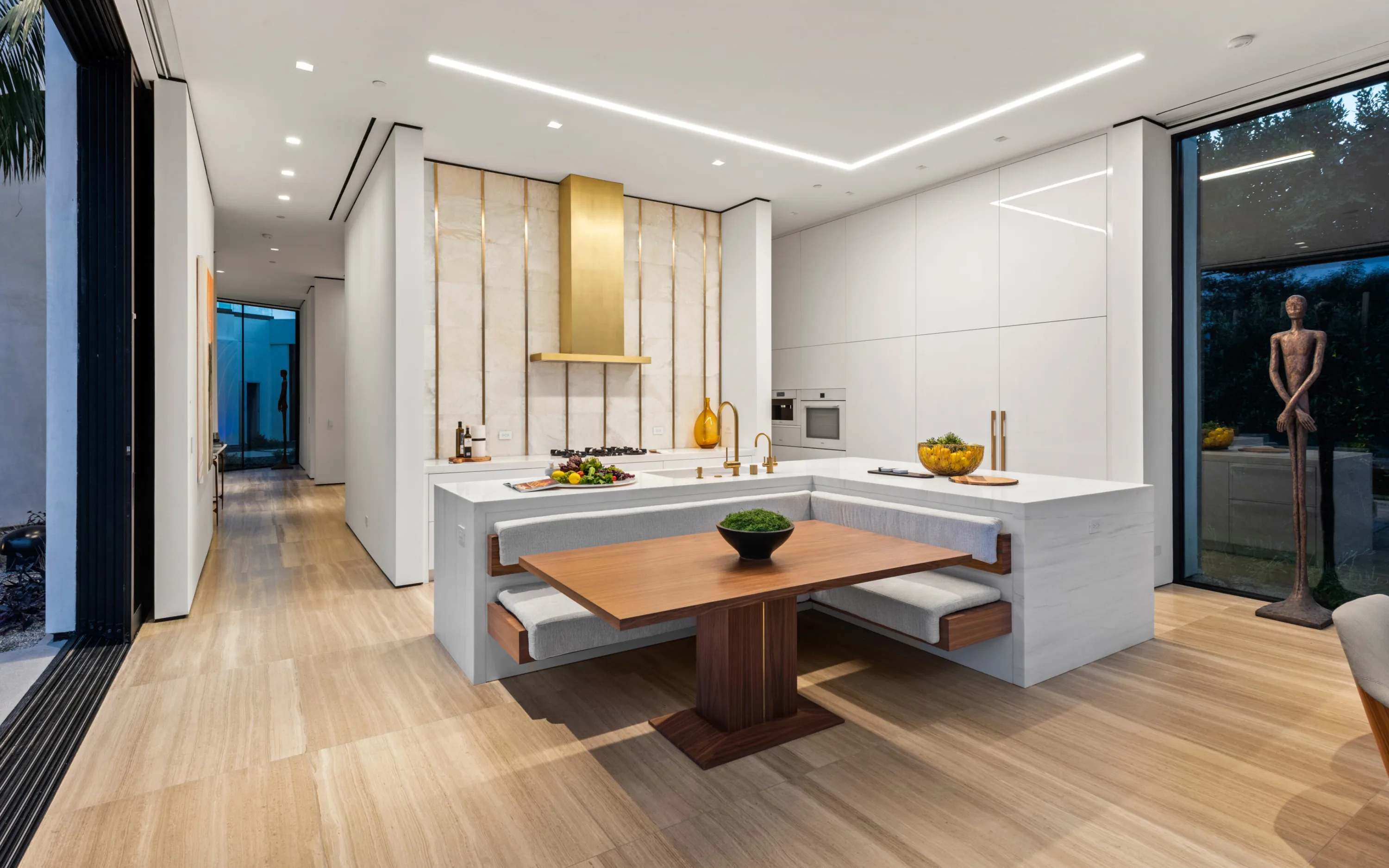 Chef's kitchen with brass hood, onyx-panelled wall and a built-in banquette around a walnut table
