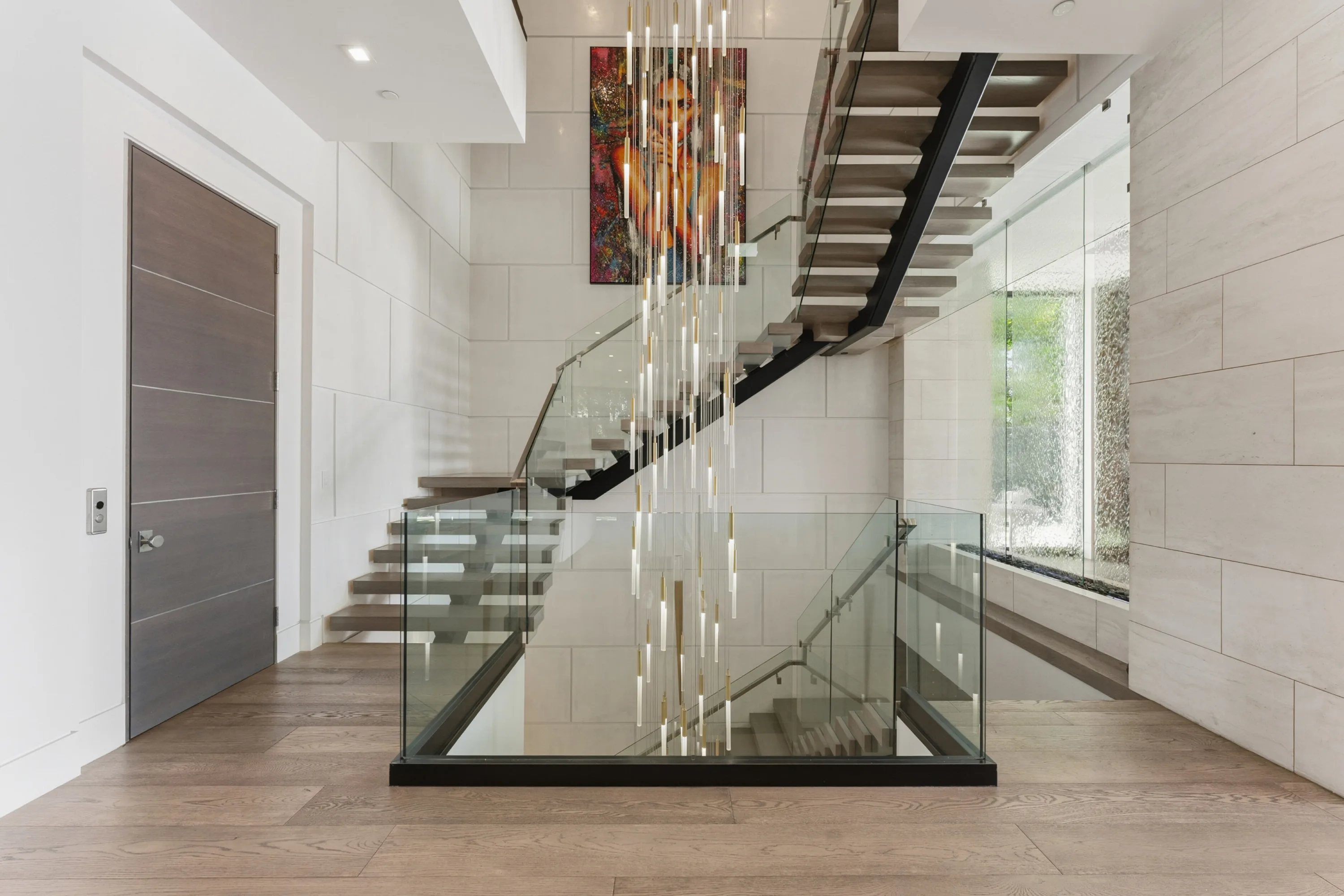 Entry hall stairwell with floating treads, glass balustrade and a cascade of slim brass pendants