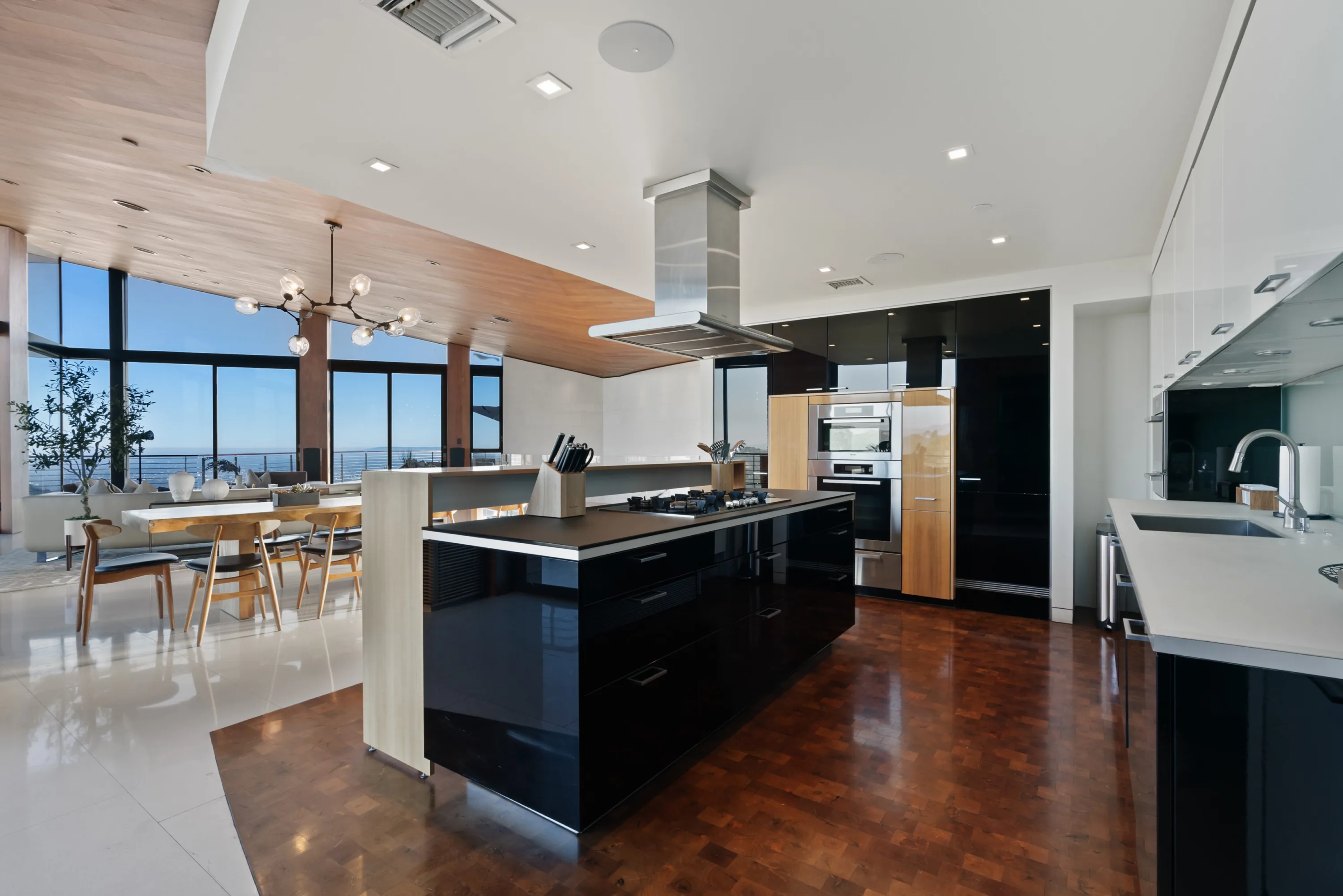 Black gloss cooking island with gas range and extractor, dining room and ocean-blue horizon beyond