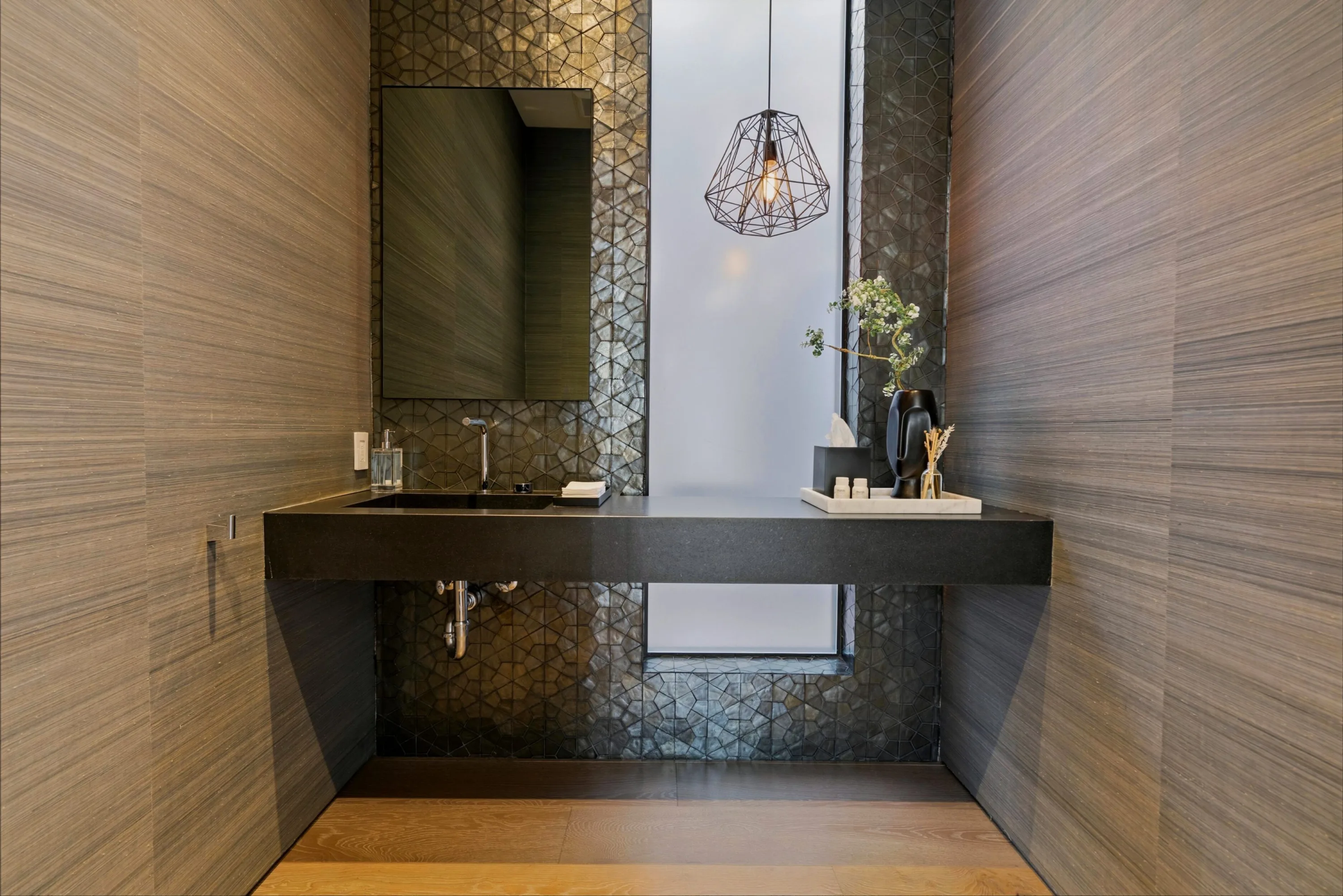 Powder room with floating black stone basin, mosaic tile and a faceted pendant over a slot window
