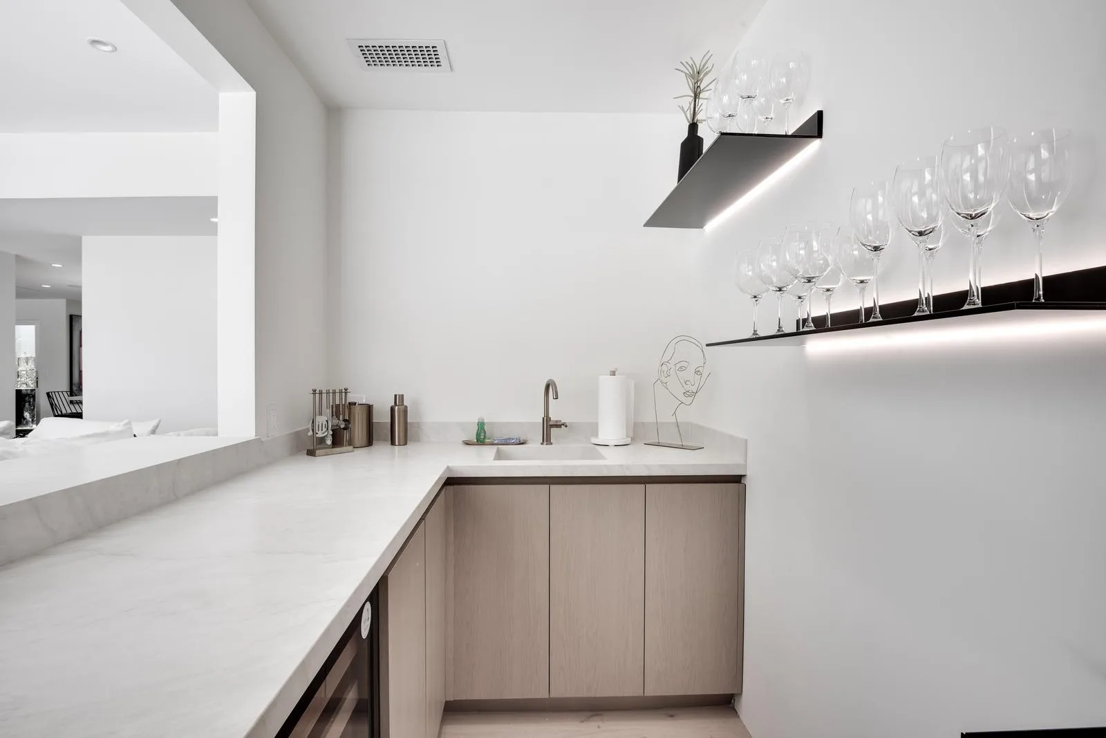 Wet bar with marble counter, prep sink and backlit shelves of wine glasses