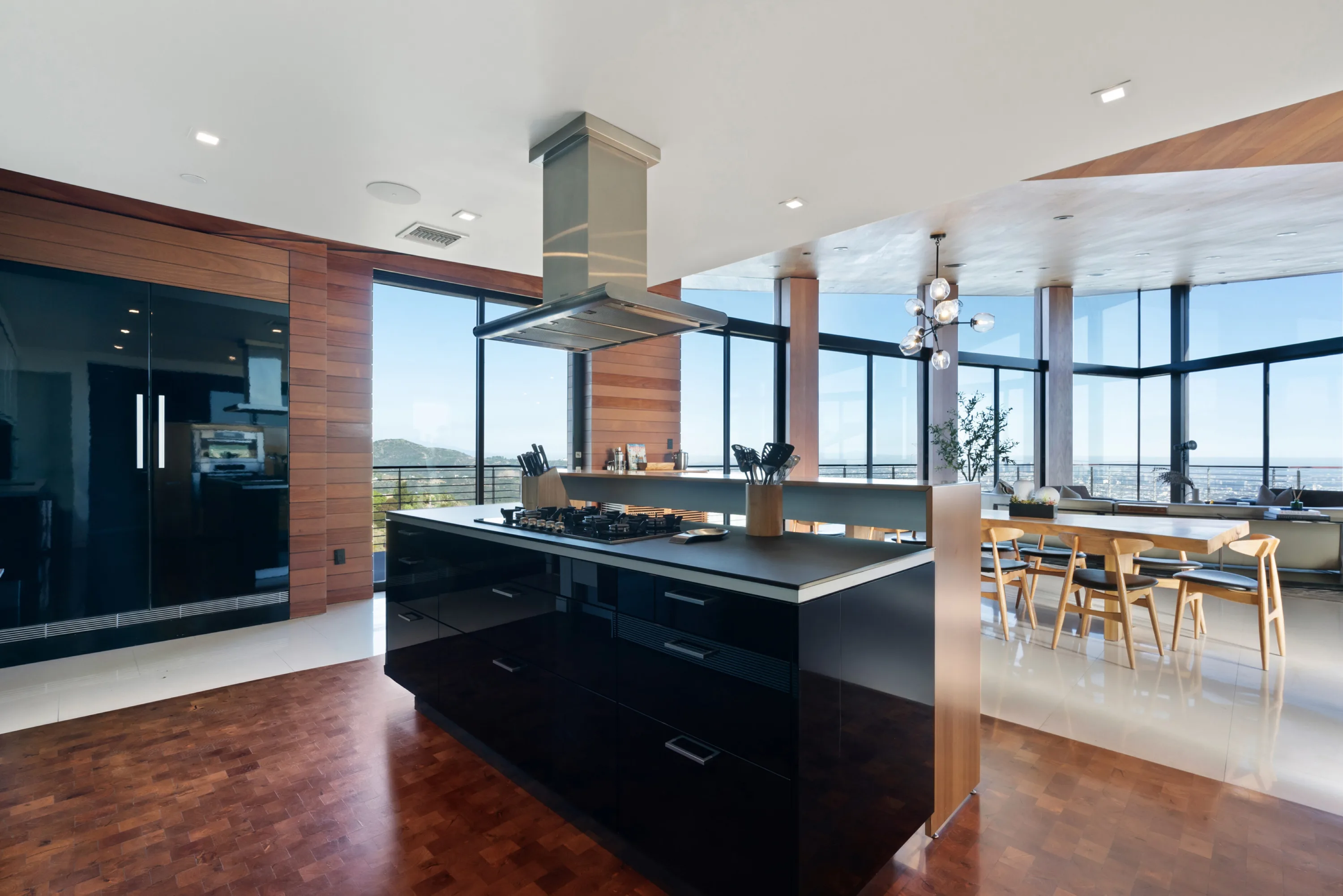 Kitchen island viewed toward the dining table, floor-to-ceiling glass framing the hills