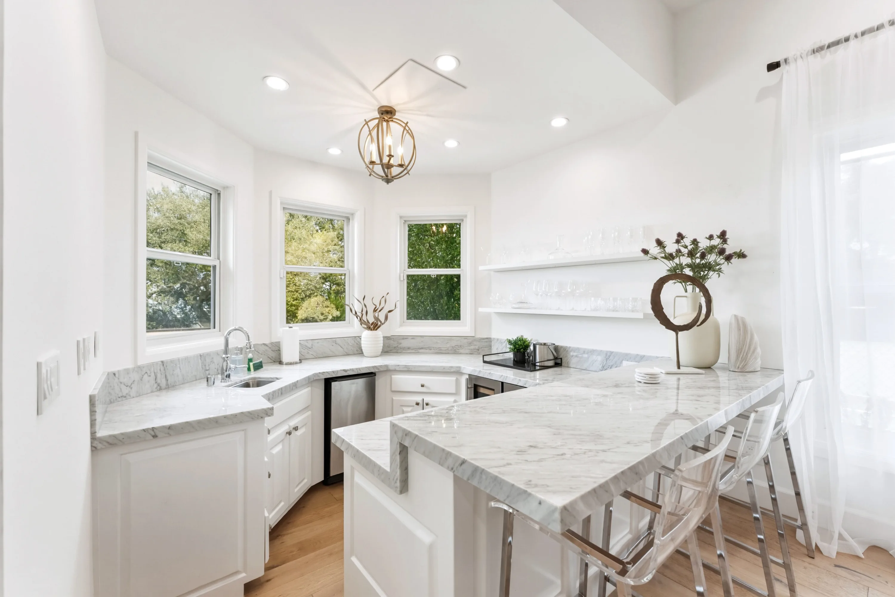 Secondary kitchenette with marble peninsula, acrylic bar stools and corner windows onto greenery