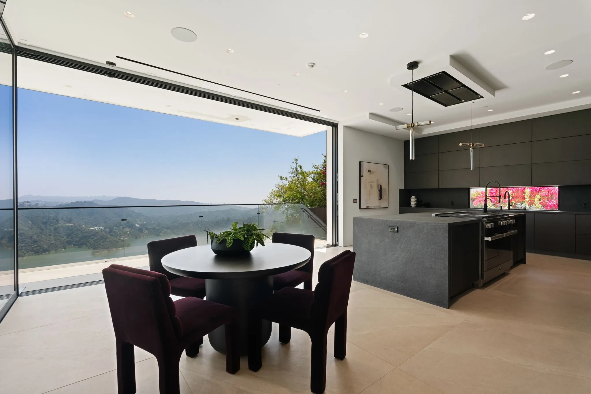 Breakfast table for four beside sliding glass doors framing the reservoir, with the dark chef's kitchen behind