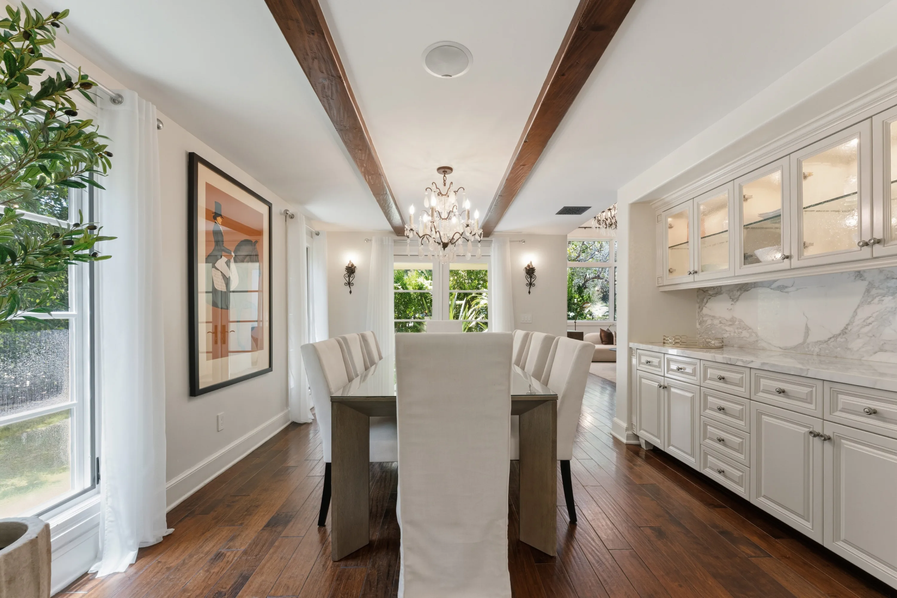 Formal dining room with beamed ceiling, crystal chandelier and marble-topped butler's pantry beside garden windows