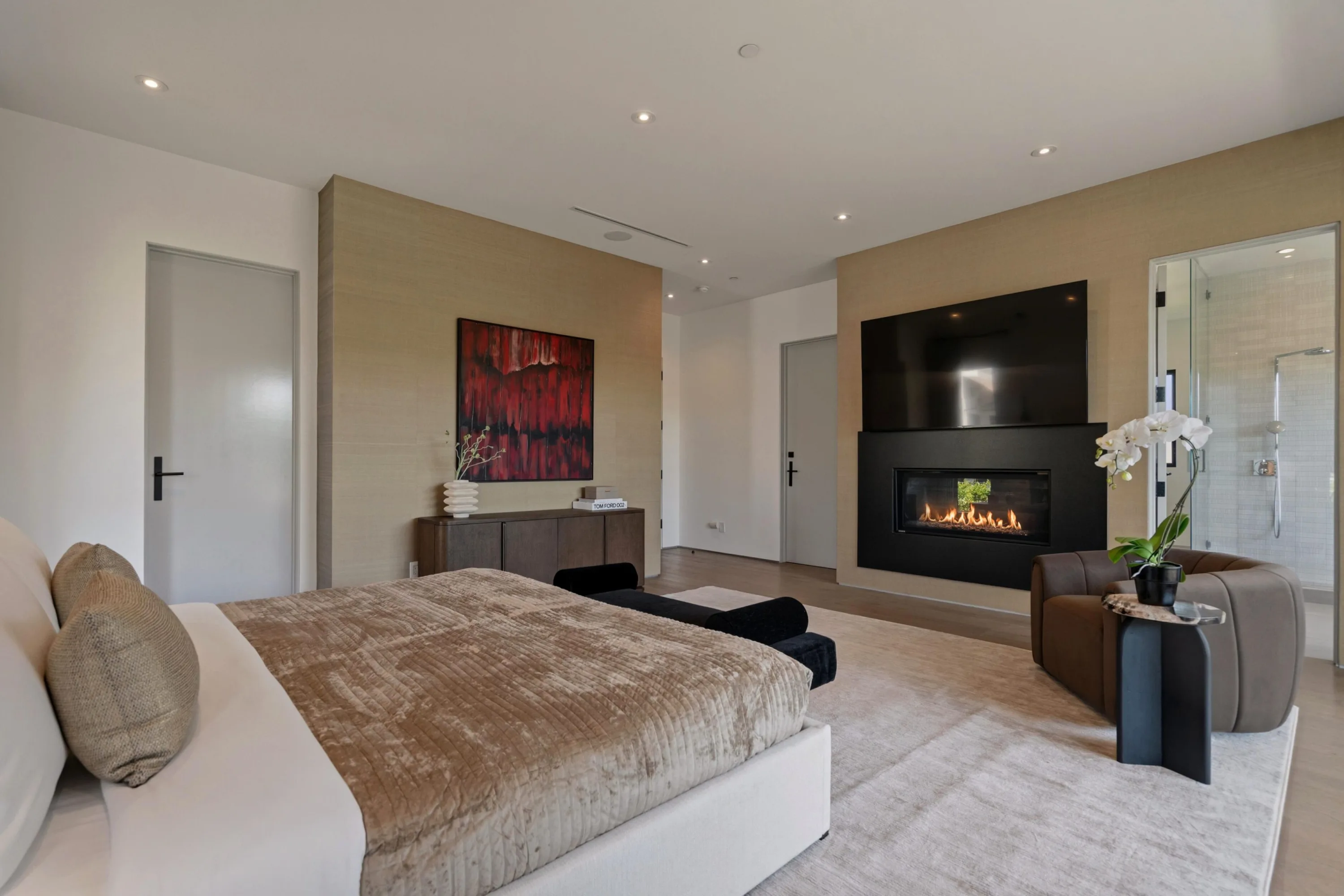 Primary suite with linear fireplace below a wall-mounted TV and glimpse of the ensuite shower