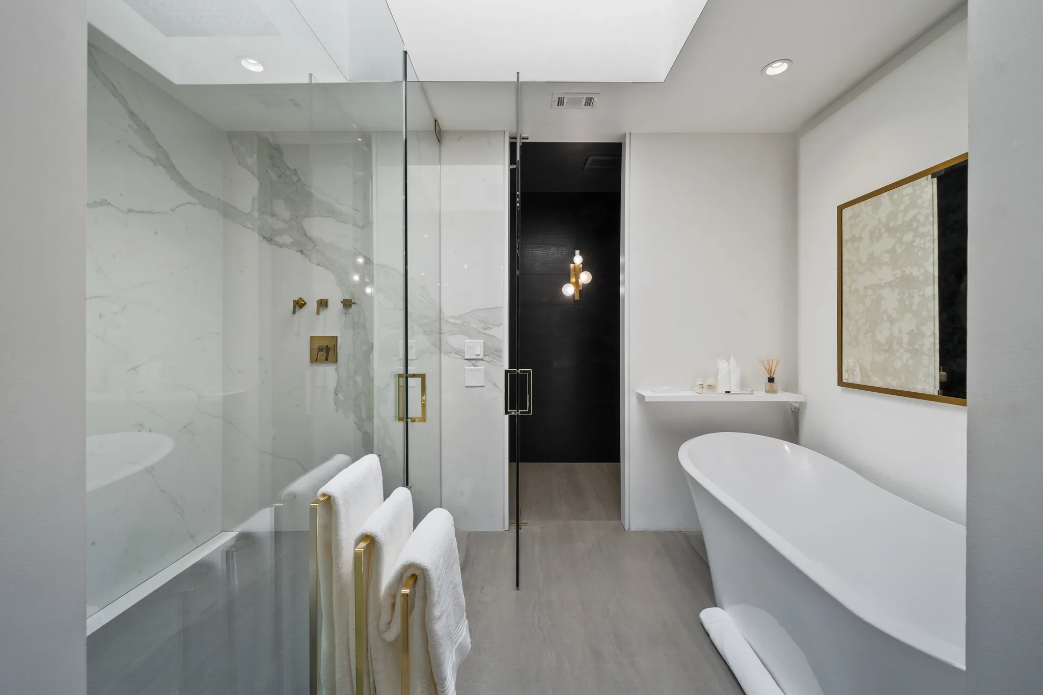 Freestanding soaking tub beside a marble walk-in shower and folded towels on a brass rail