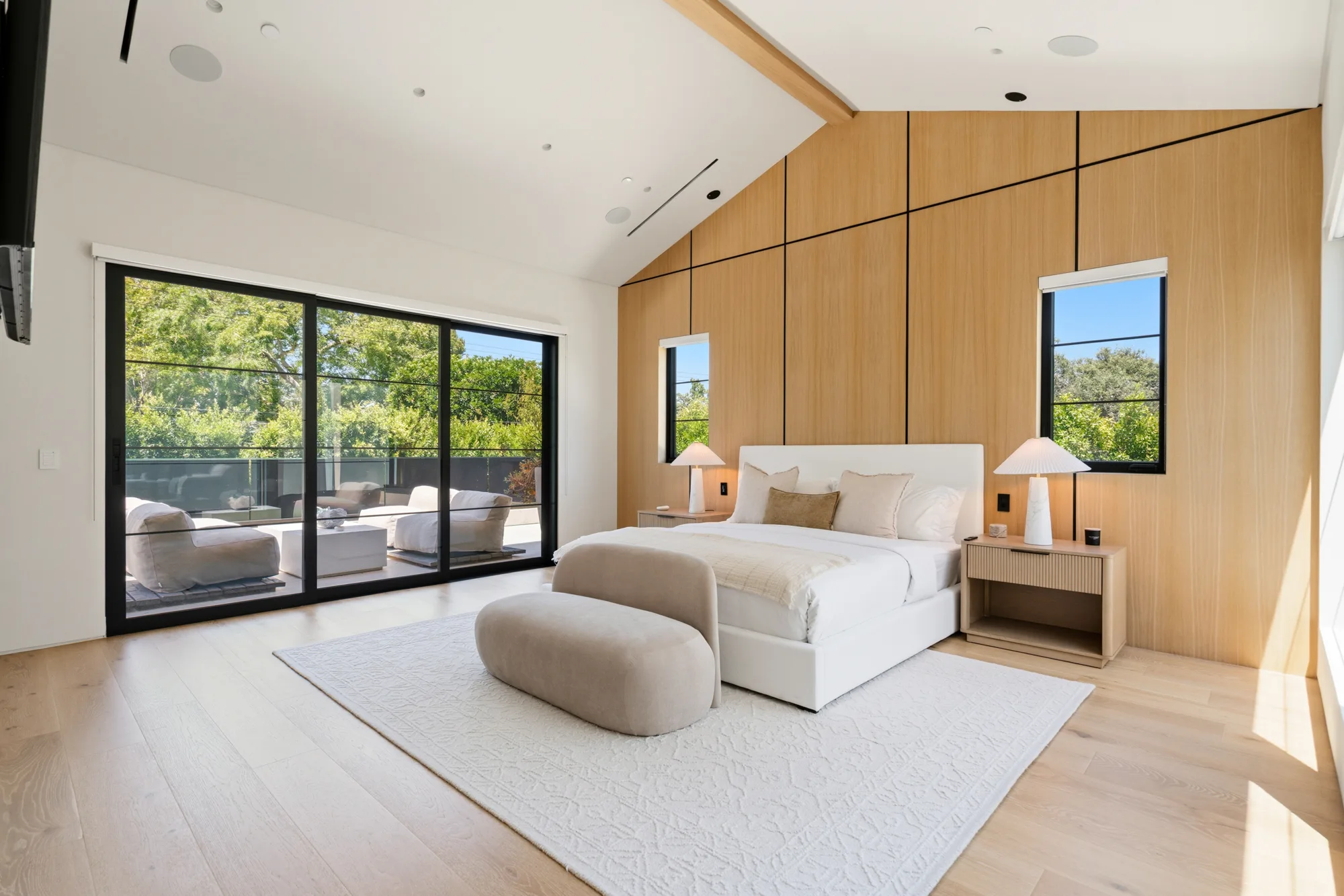 Primary suite under a vaulted ceiling, oak feature wall and sliding doors to a furnished balcony