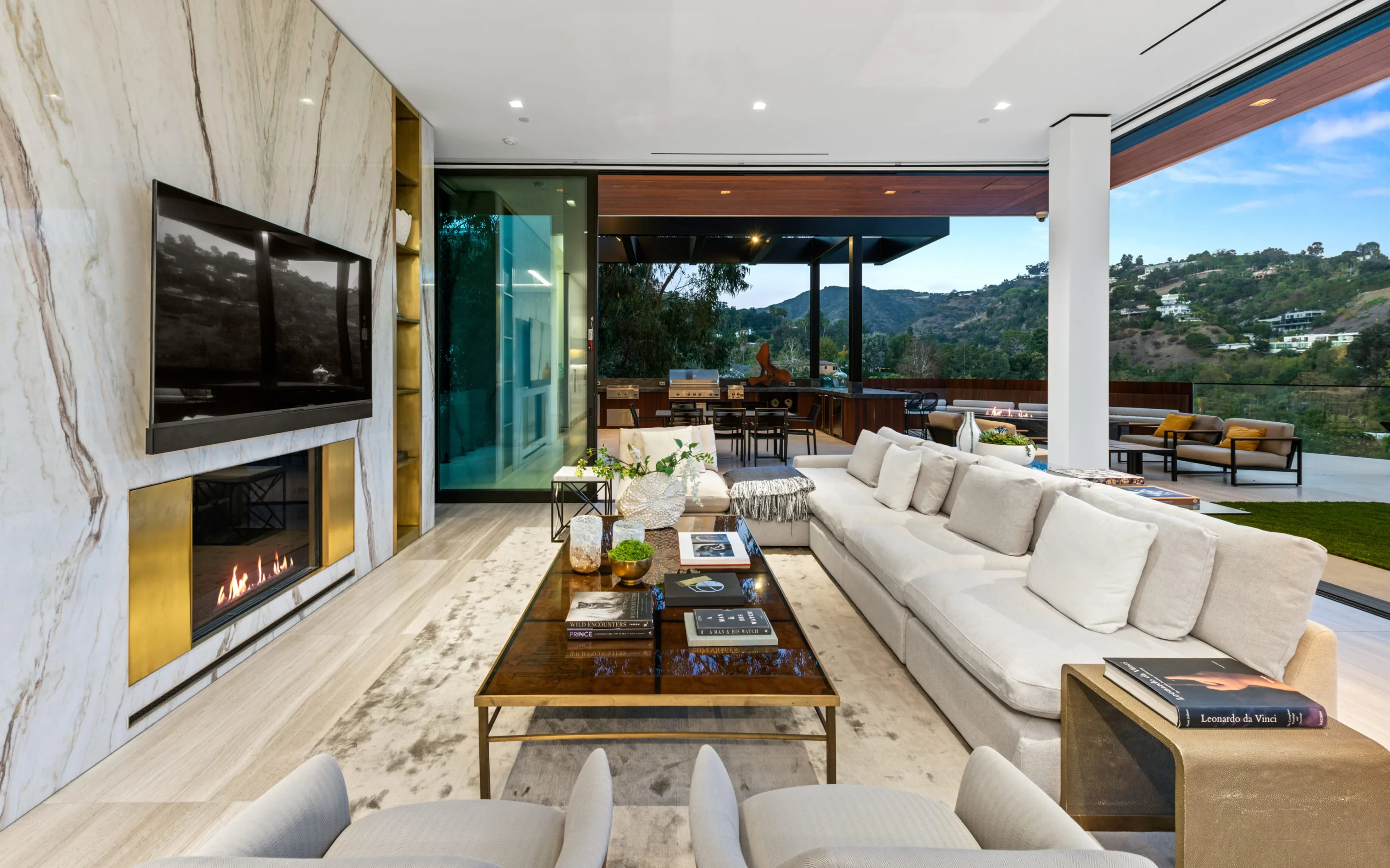 Family lounge with marble fireplace and wall-mounted TV, sliding walls open to the outdoor kitchen