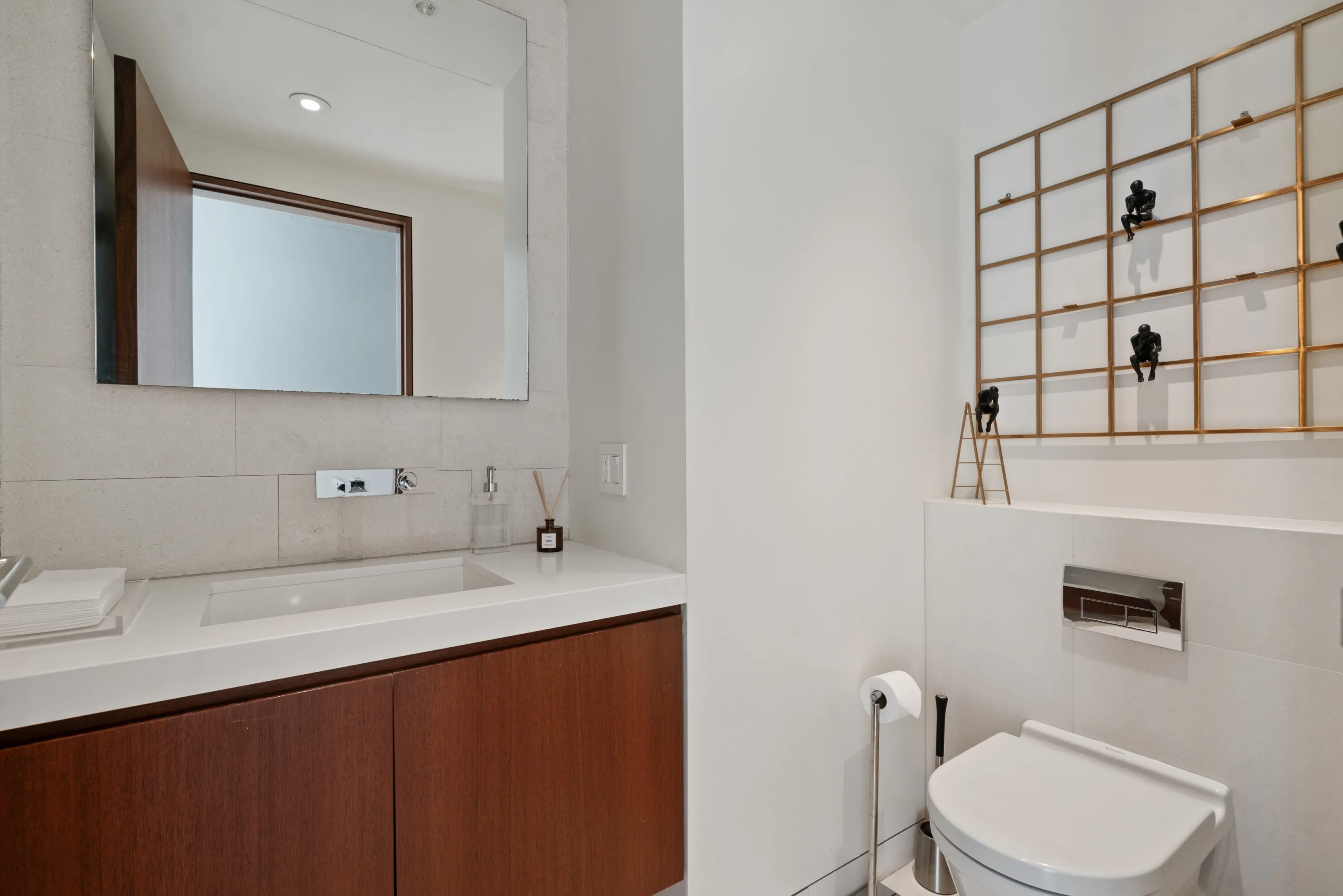 Powder room with floating walnut vanity, wide mirror and a gilded grid shelf holding small figurines
